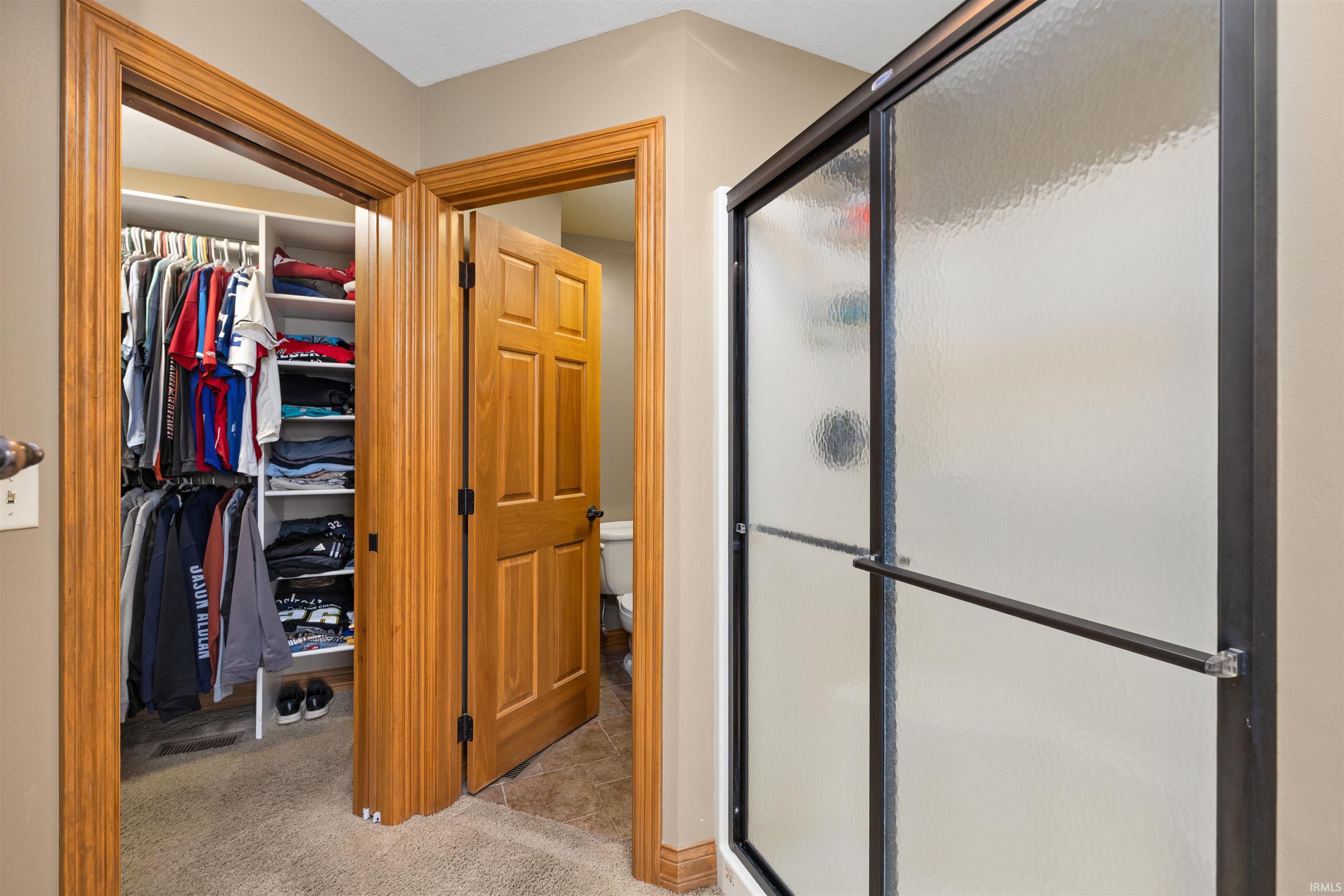 Bathroom featuring a shower stall, light carpet, and a spacious closet
