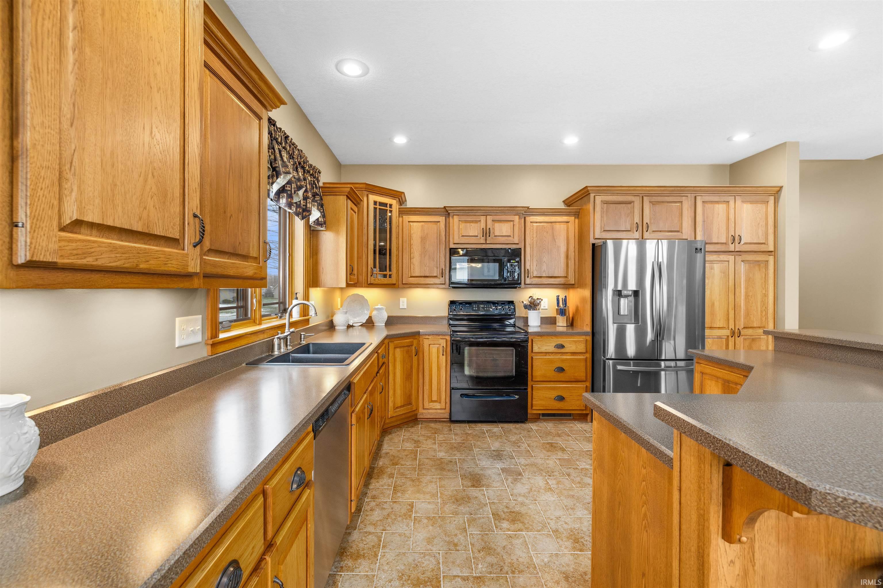 Kitchen with glass insert cabinets, wood finish cabinetry, black appliances, stone finish flooring, and dark countertops