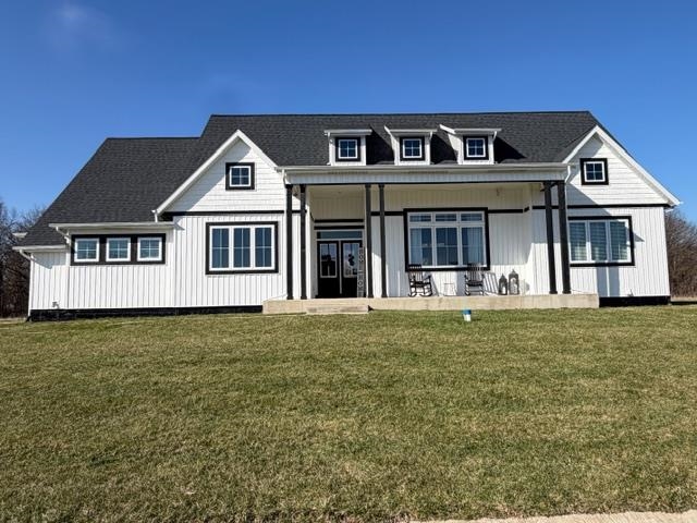 Modern farmhouse style home with a porch, a front lawn, board and batten siding, and a shingled roof