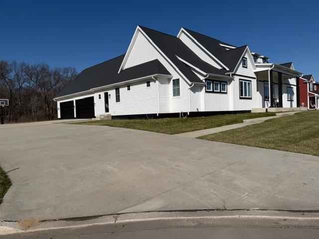 View of side of property with a garage, concrete driveway, a porch, and a lawn