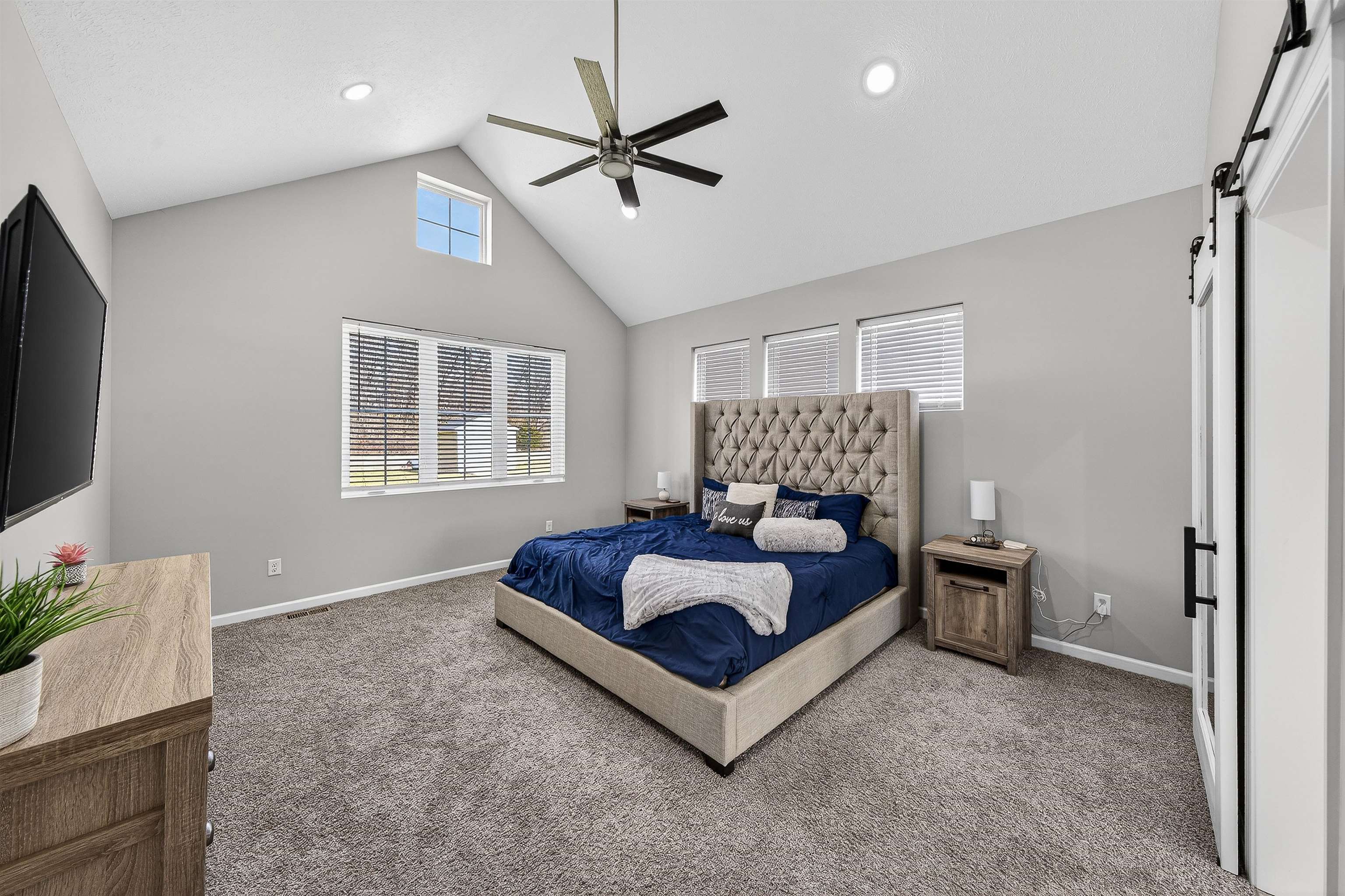 Bedroom featuring a barn door, ceiling fan, carpet flooring, and a high ceiling