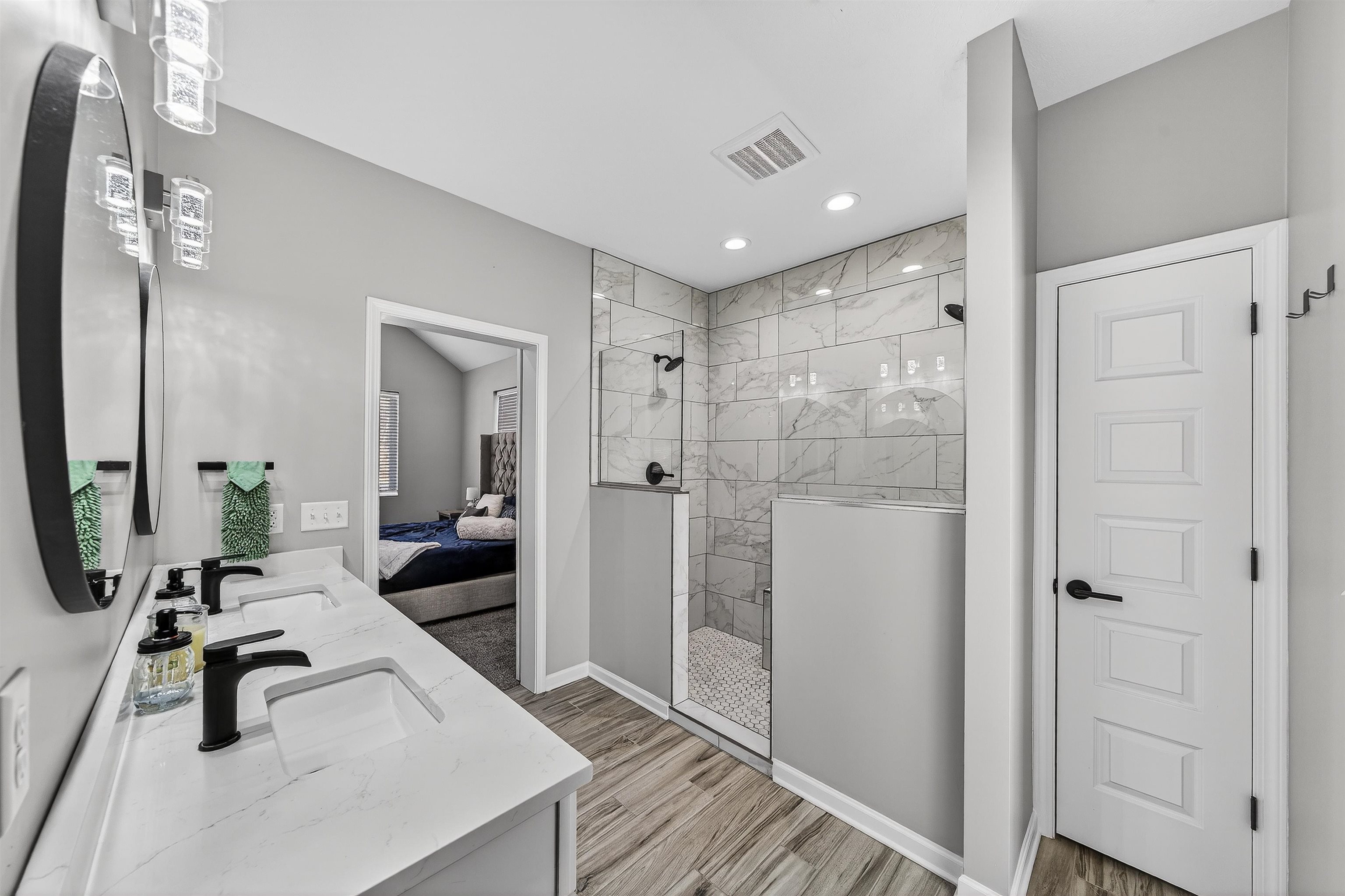 Ensuite bathroom with a walk in shower, double vanity, and light wood-style flooring