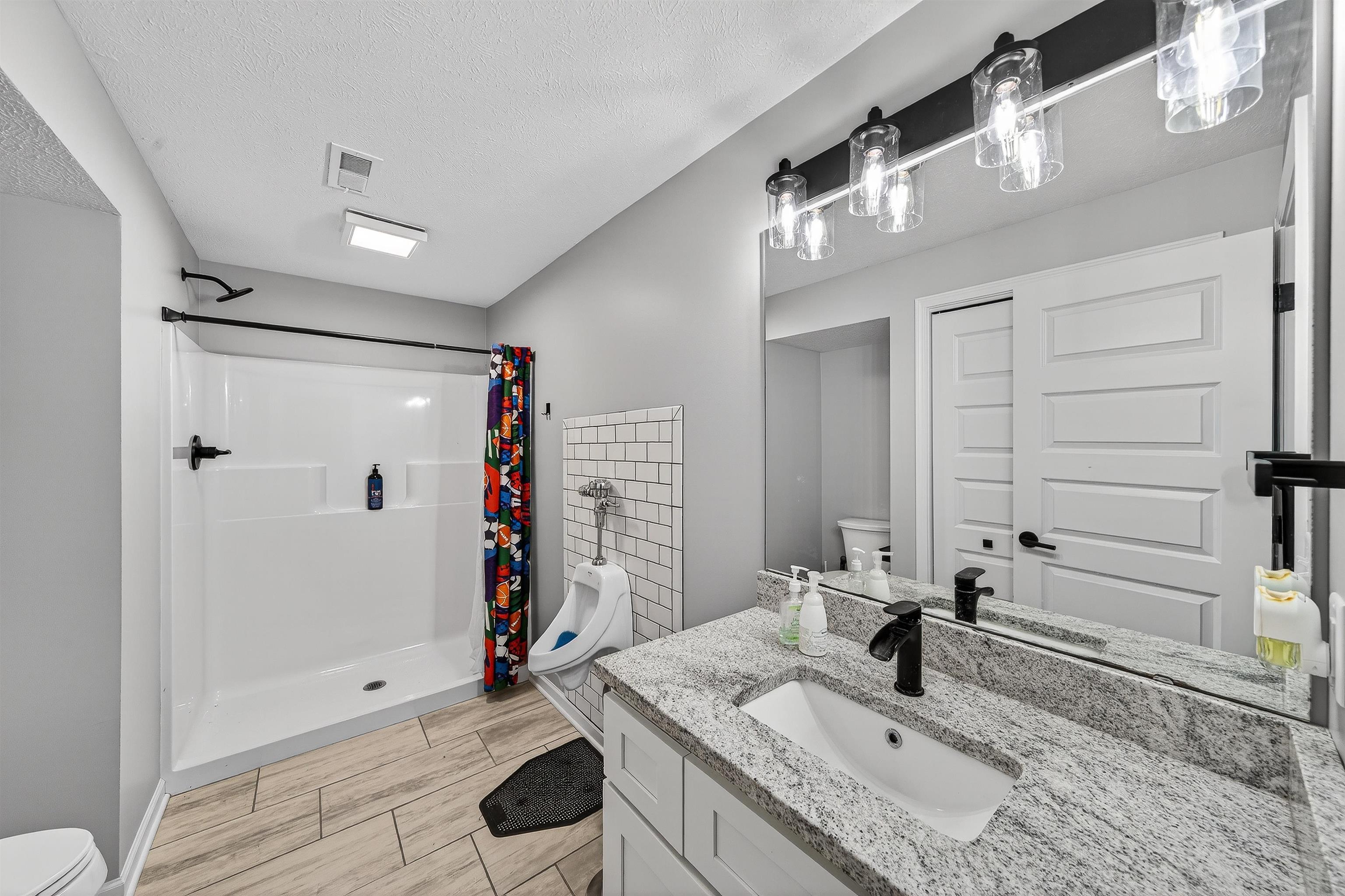 Full bath with a stall shower, vanity, a textured ceiling, and wood finish floors