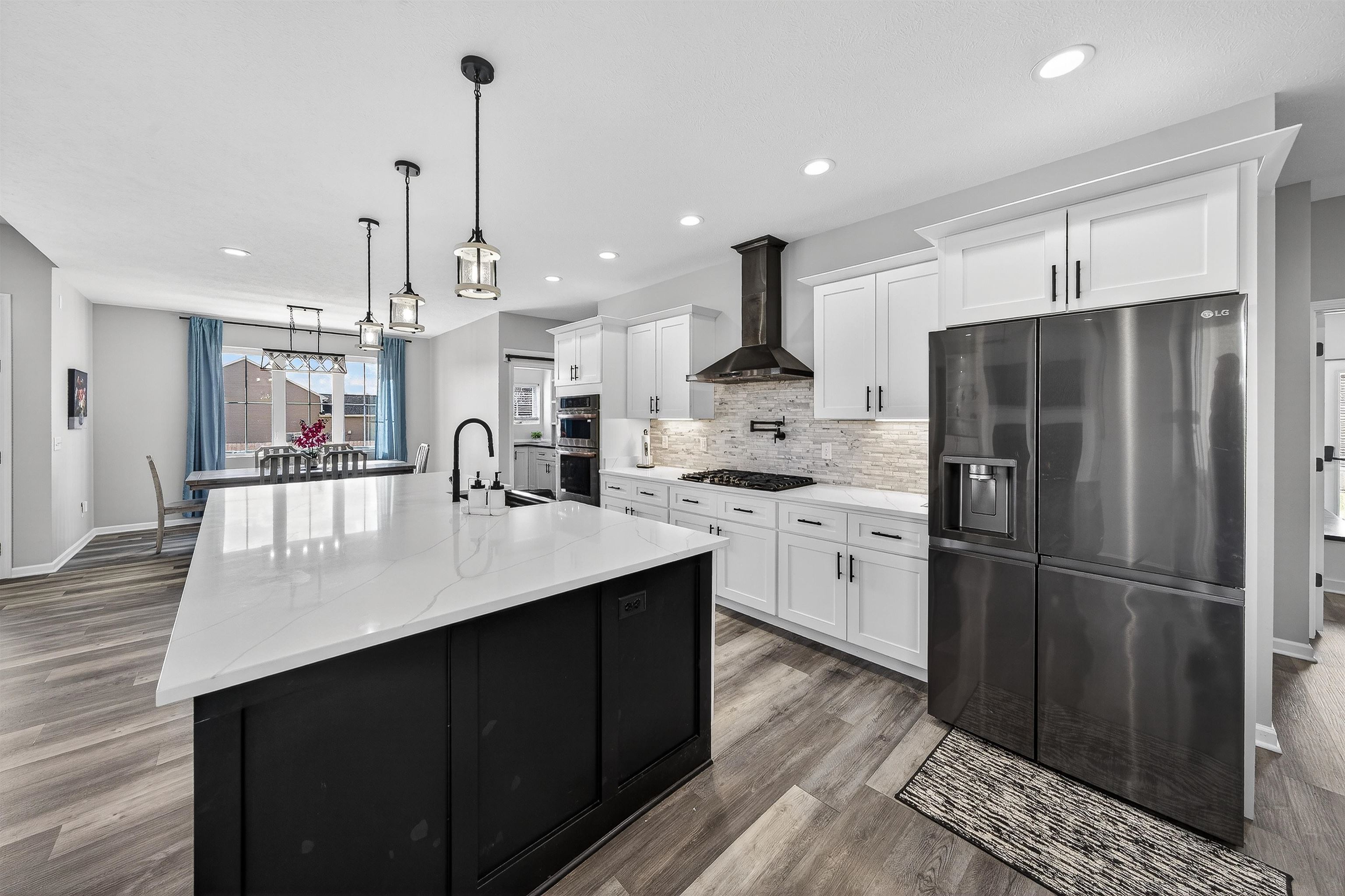 Kitchen with stainless steel appliances, a kitchen island with sink, light stone counters, dark wood-style floors, and two tone cabinetry