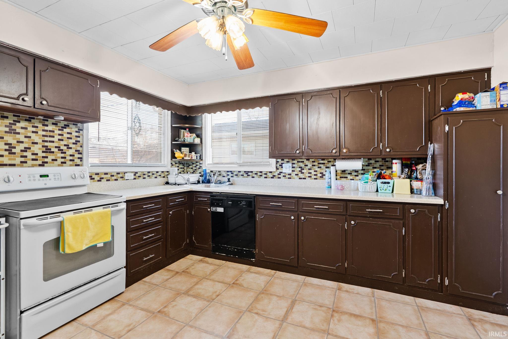 Kitchen featuring white electric range oven, dark wood finish cabinets, a ceiling fan, black dishwasher, and light countertops