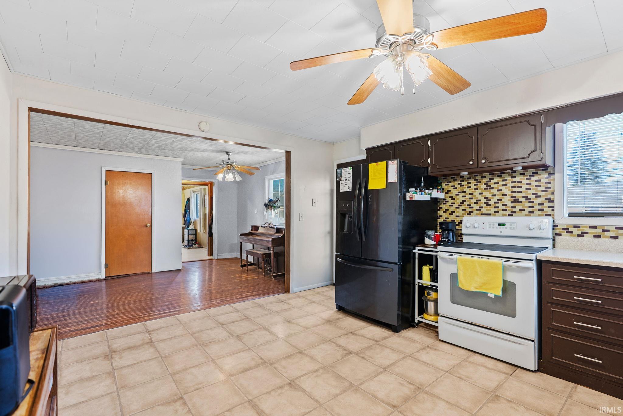 Kitchen featuring a ceiling fan, dark wood finish cabinets, white electric range oven, light countertops, and black fridge