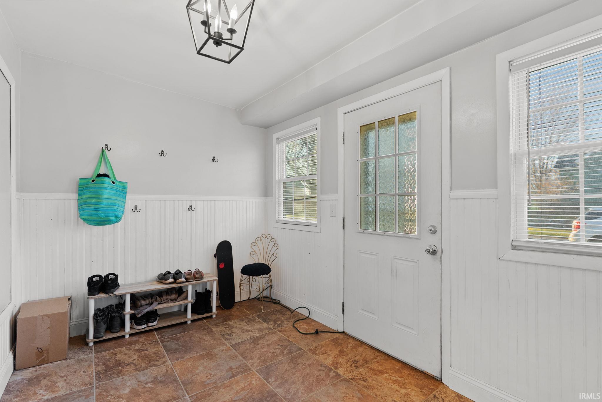 Mudroom with a wainscoted wall, a chandelier, and dark stone finish flooring