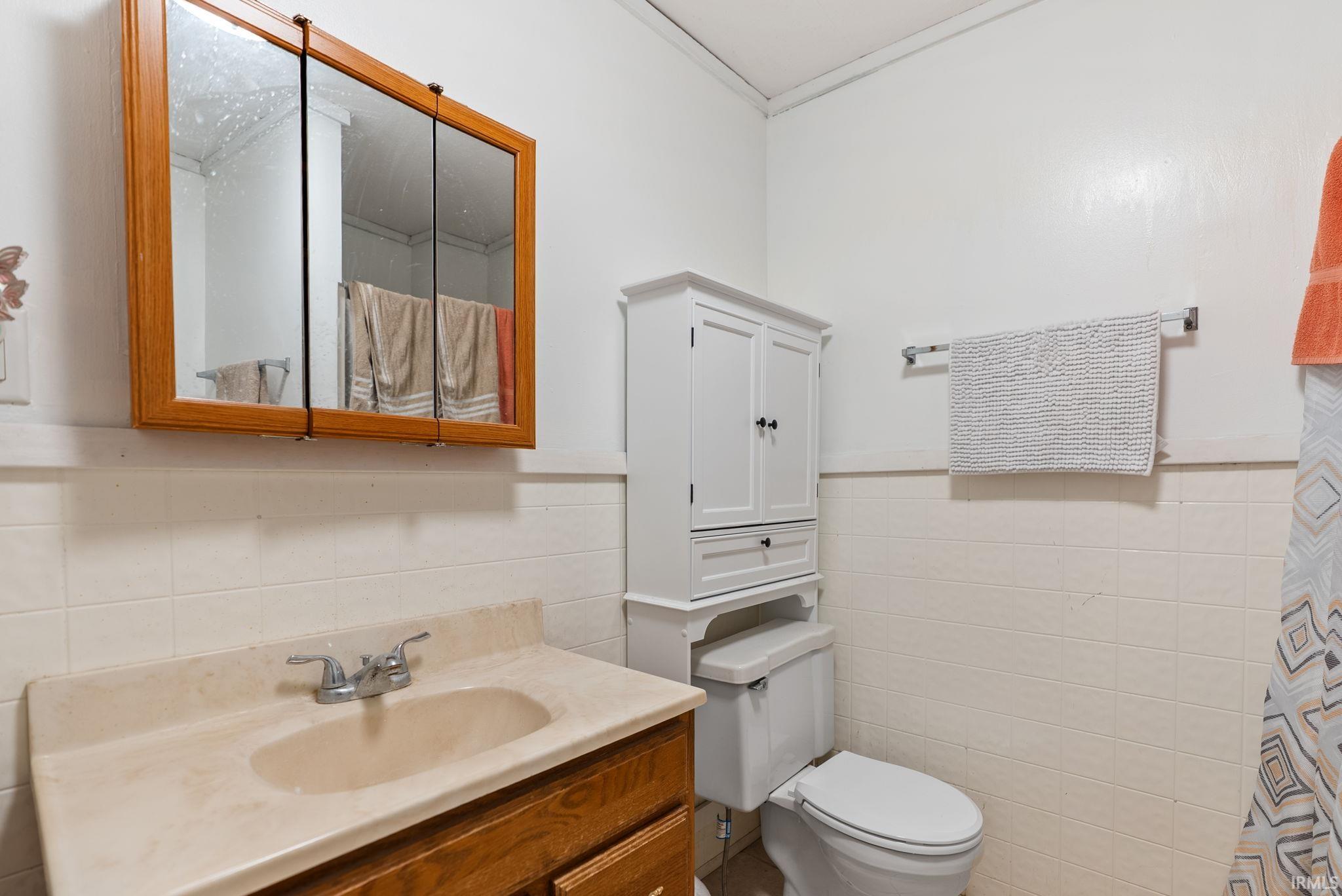 Bathroom with vanity, a shower with shower curtain, a wainscoted wall, and tile walls