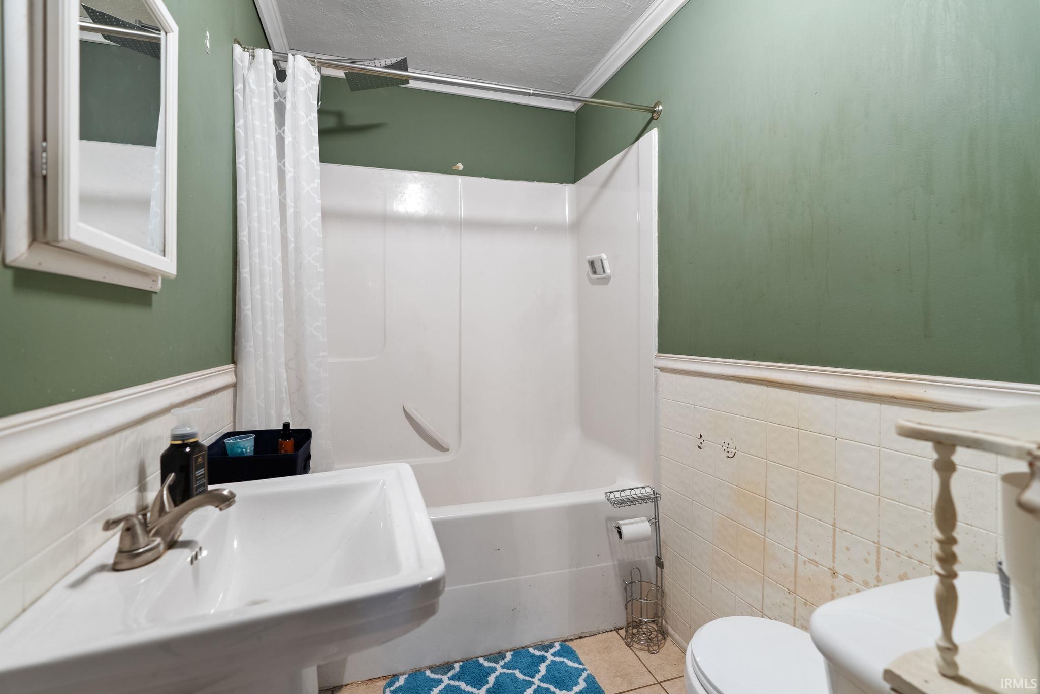 Bathroom featuring wainscoting, shower / bath combo with shower curtain, a textured ceiling, tile walls, and ornamental molding