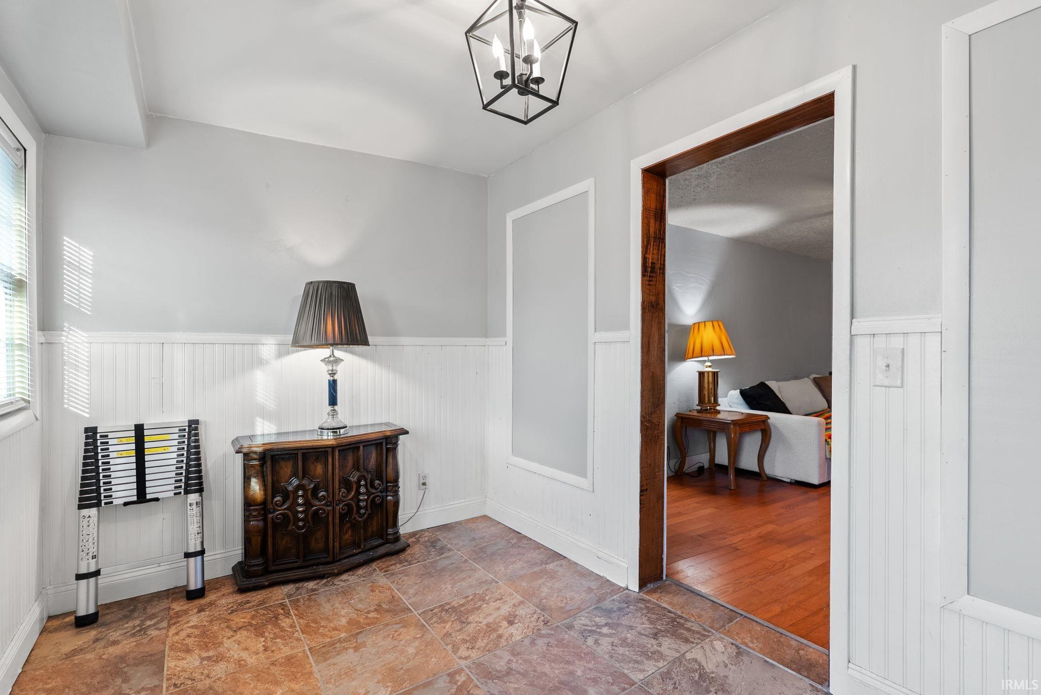 Hall with stone finish flooring, a chandelier, and wainscoting