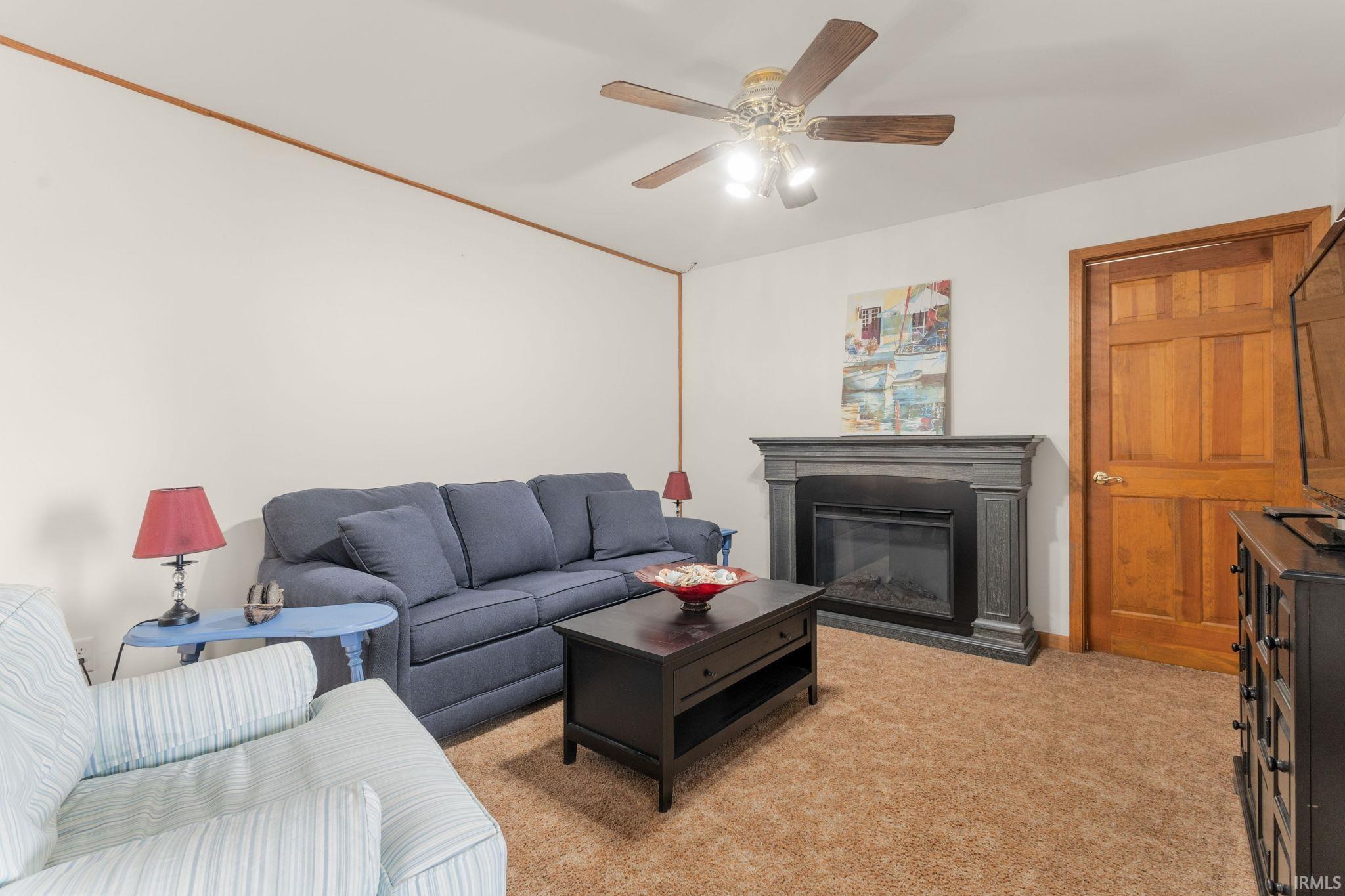Living room with light carpet, a glass covered fireplace, and a ceiling fan