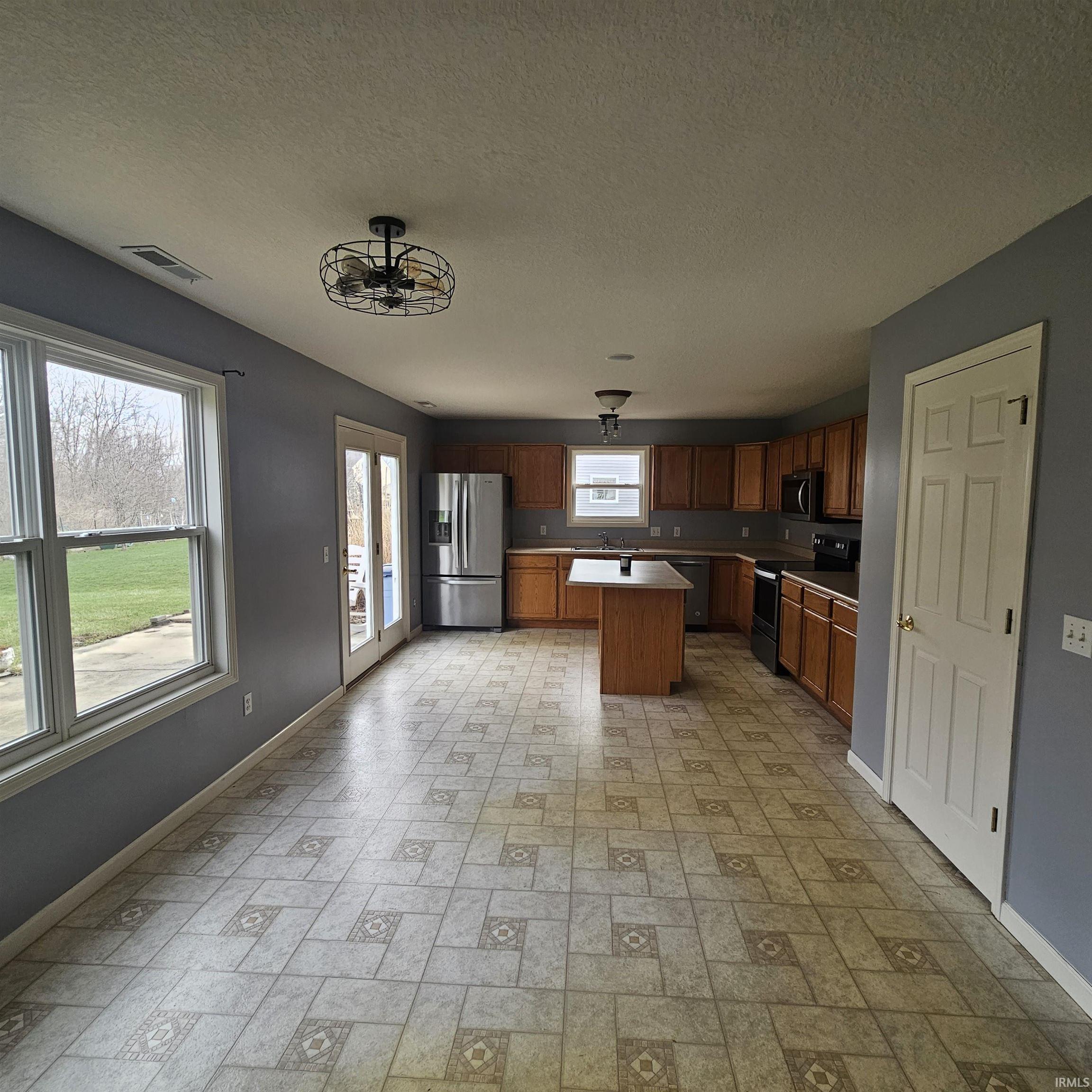 Kitchen featuring light countertops, stainless steel appliances, a center island, wood finish cabinetry, and a textured ceiling