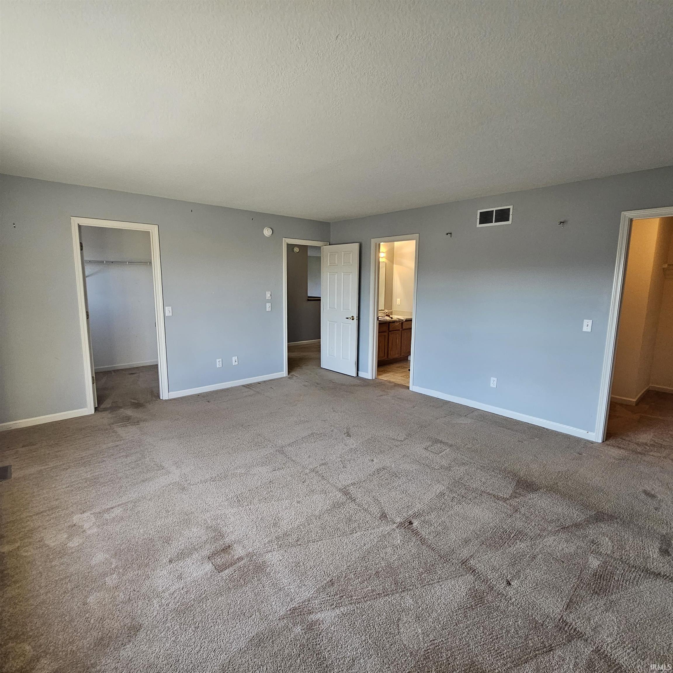 Unfurnished bedroom with a spacious closet, carpet, ensuite bathroom, and a textured ceiling