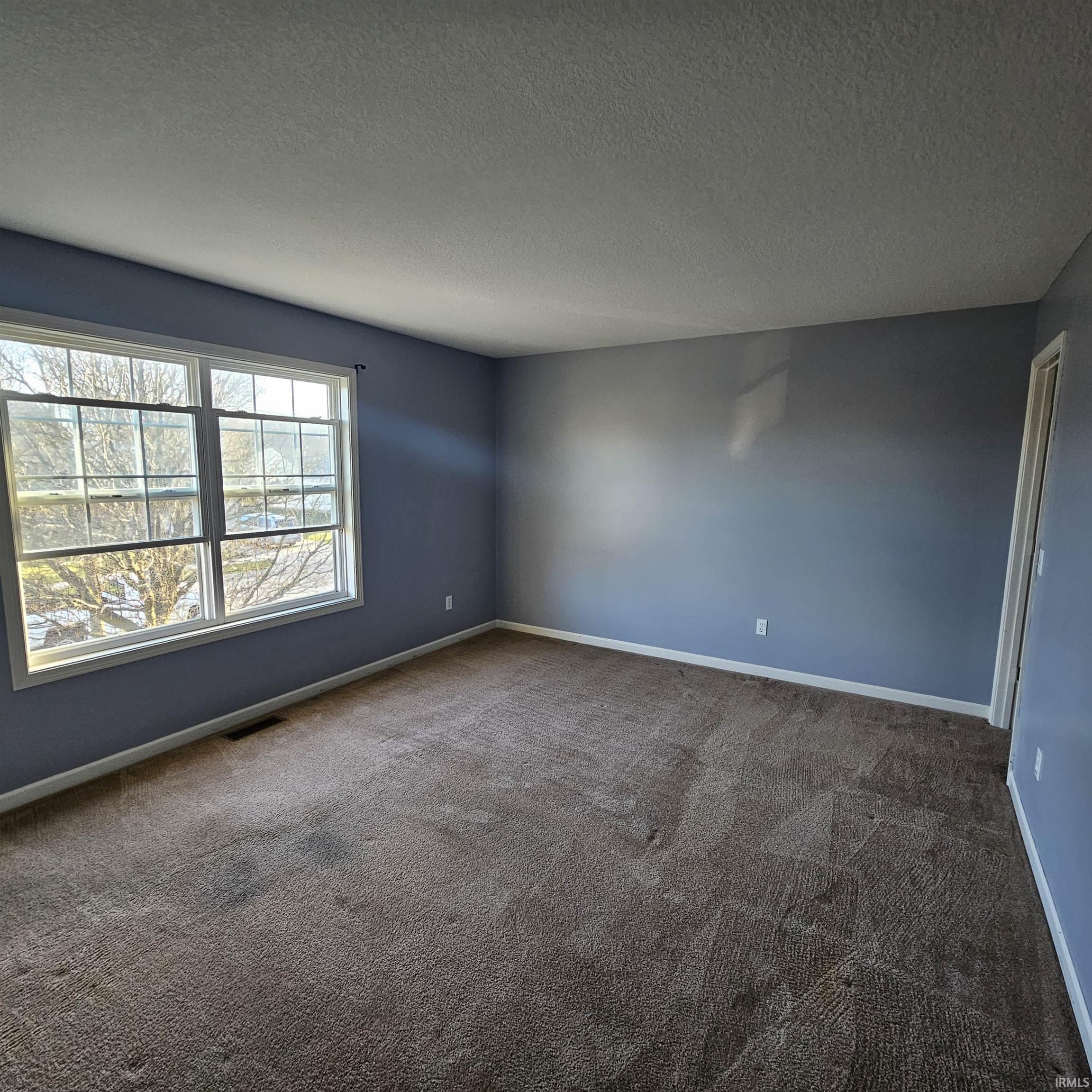 Unfurnished room featuring dark colored carpet and a textured ceiling