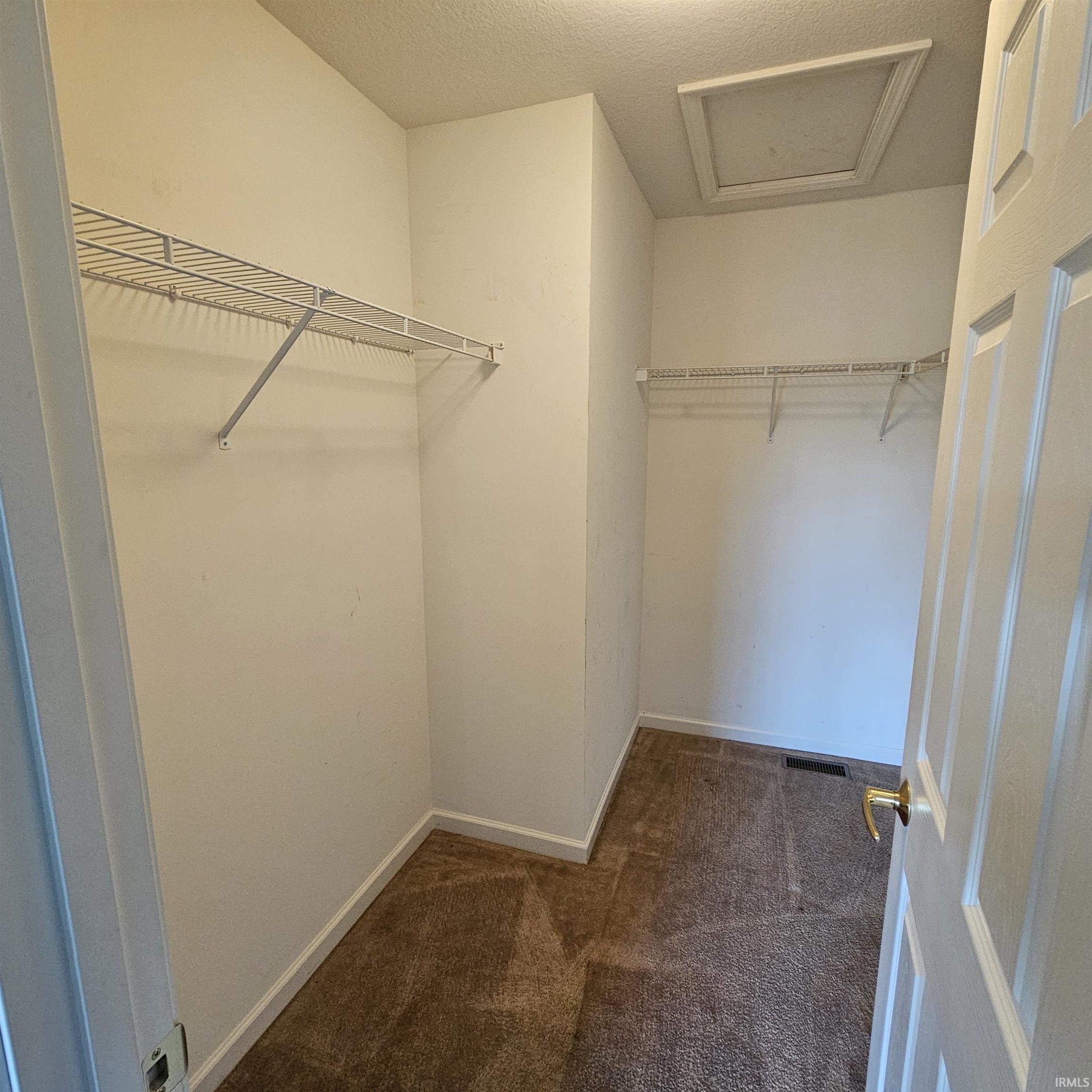 Walk in closet with attic access and dark carpet