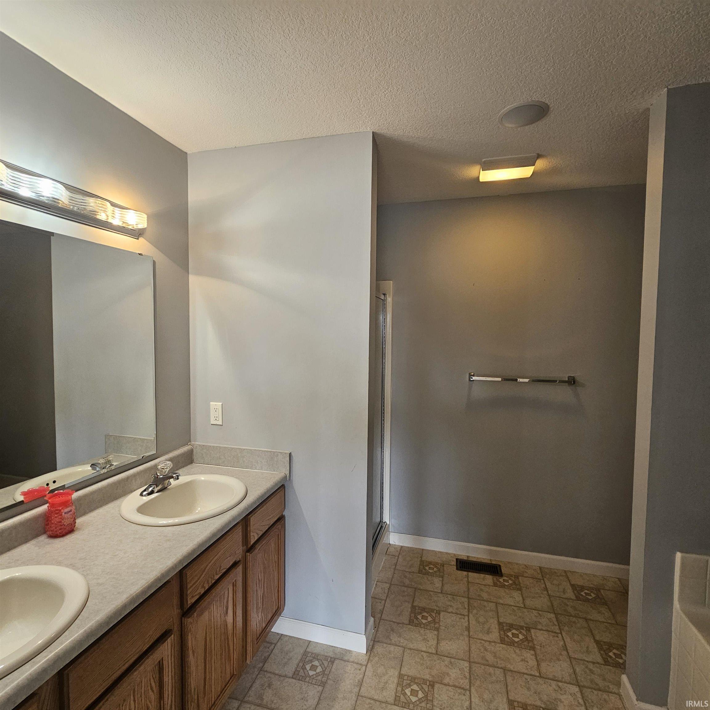 Full bath featuring light stone finish flooring, double vanity, a textured ceiling, a stall shower, and a garden tub