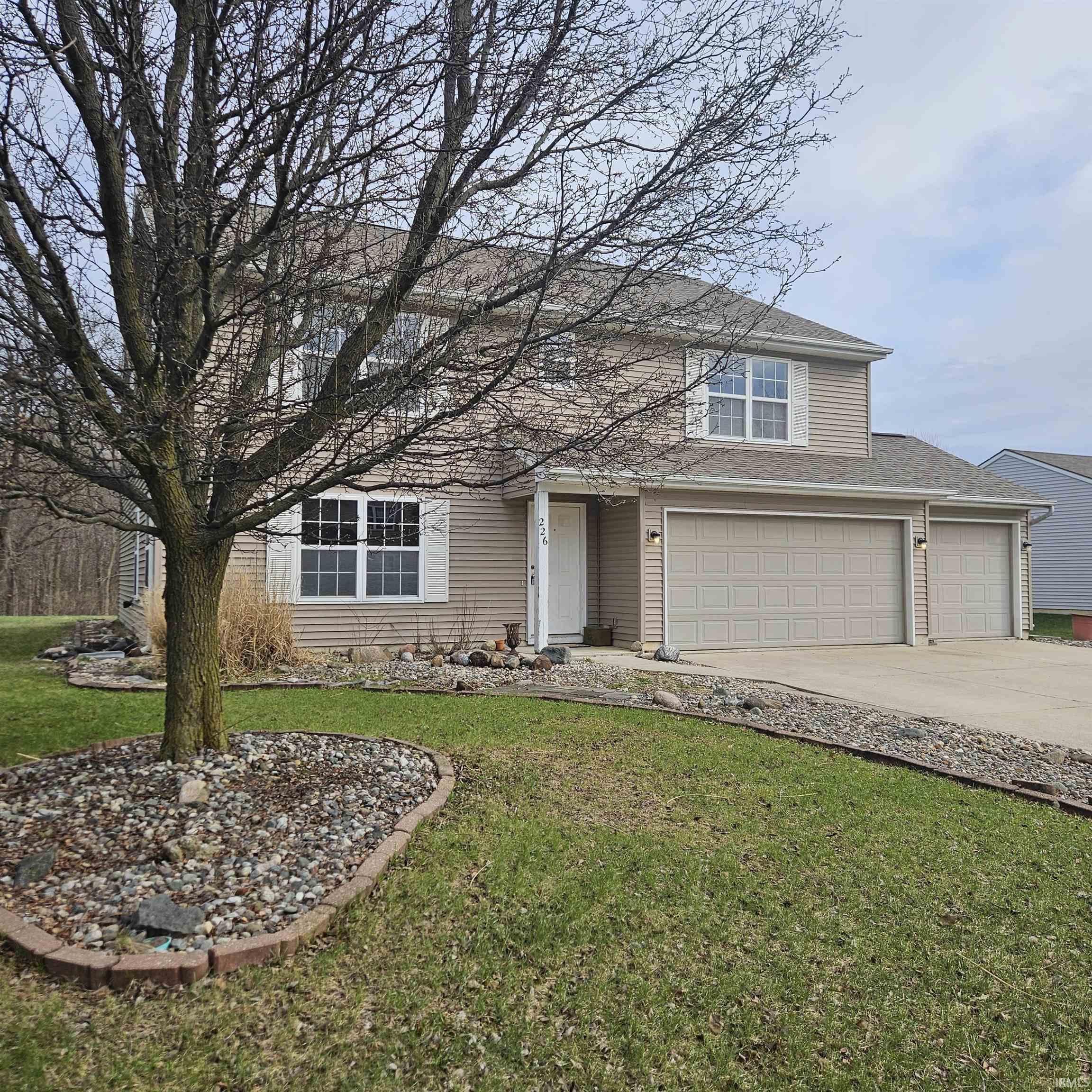 Traditional-style house with concrete driveway, a front lawn, roof with shingles, and a garage