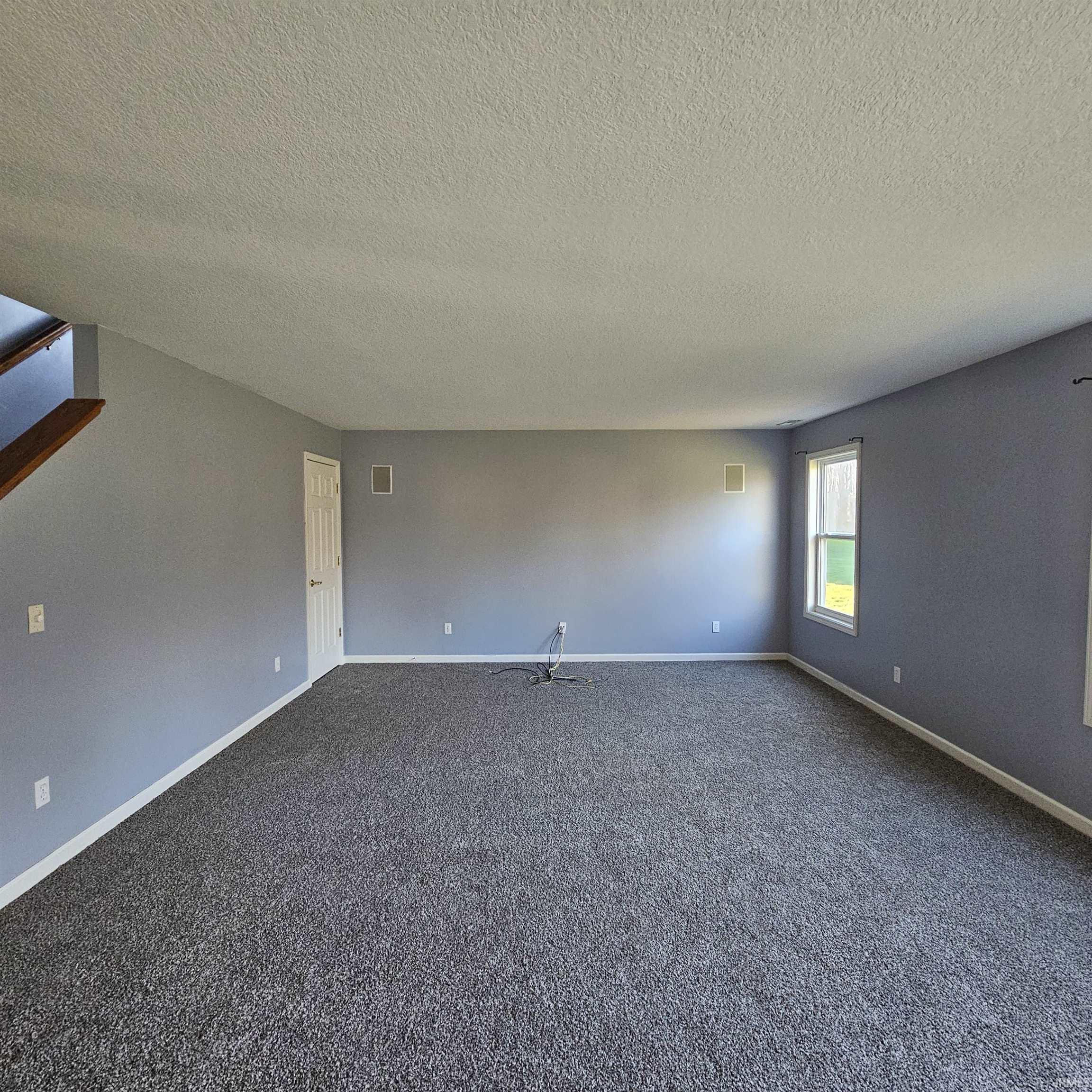 Empty room with dark carpet and a textured ceiling