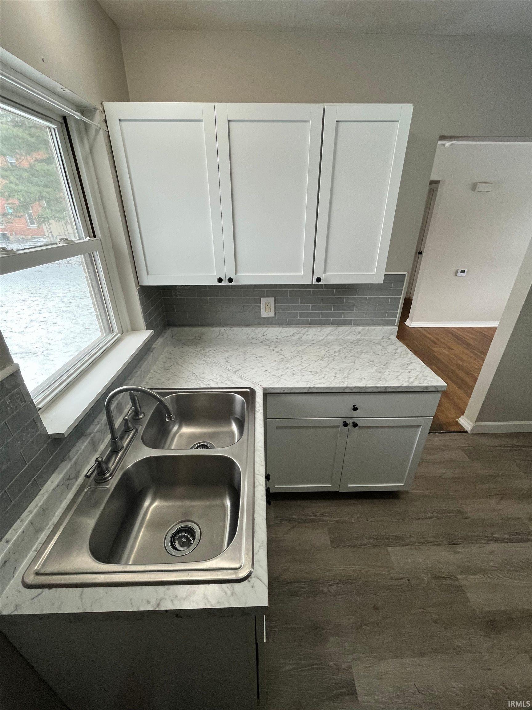 Kitchen with dark wood-style floors, light countertops, white cabinets, and decorative backsplash