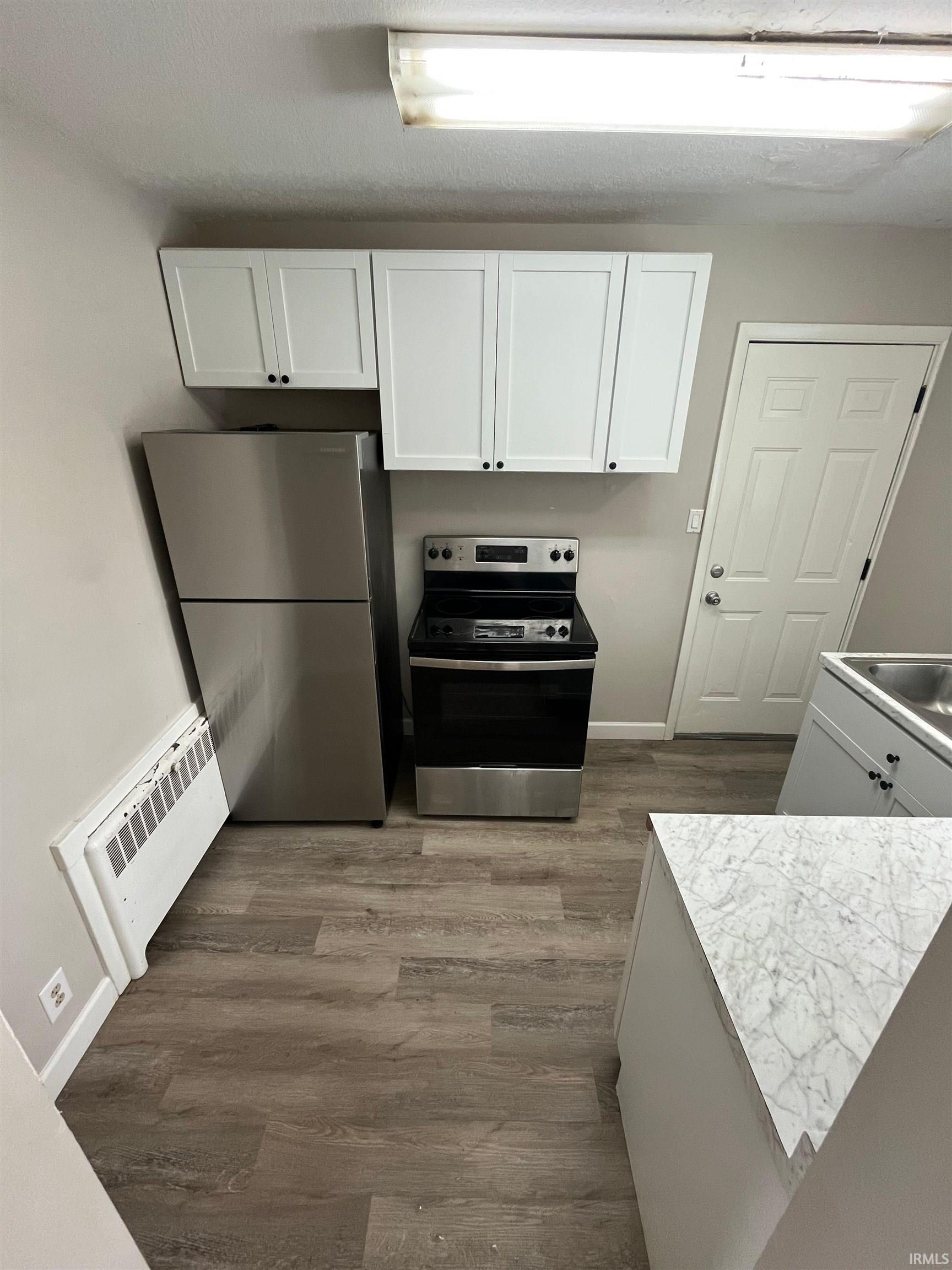 Kitchen with white cabinets, stainless steel appliances, dark wood finished floors, radiator, and light countertops