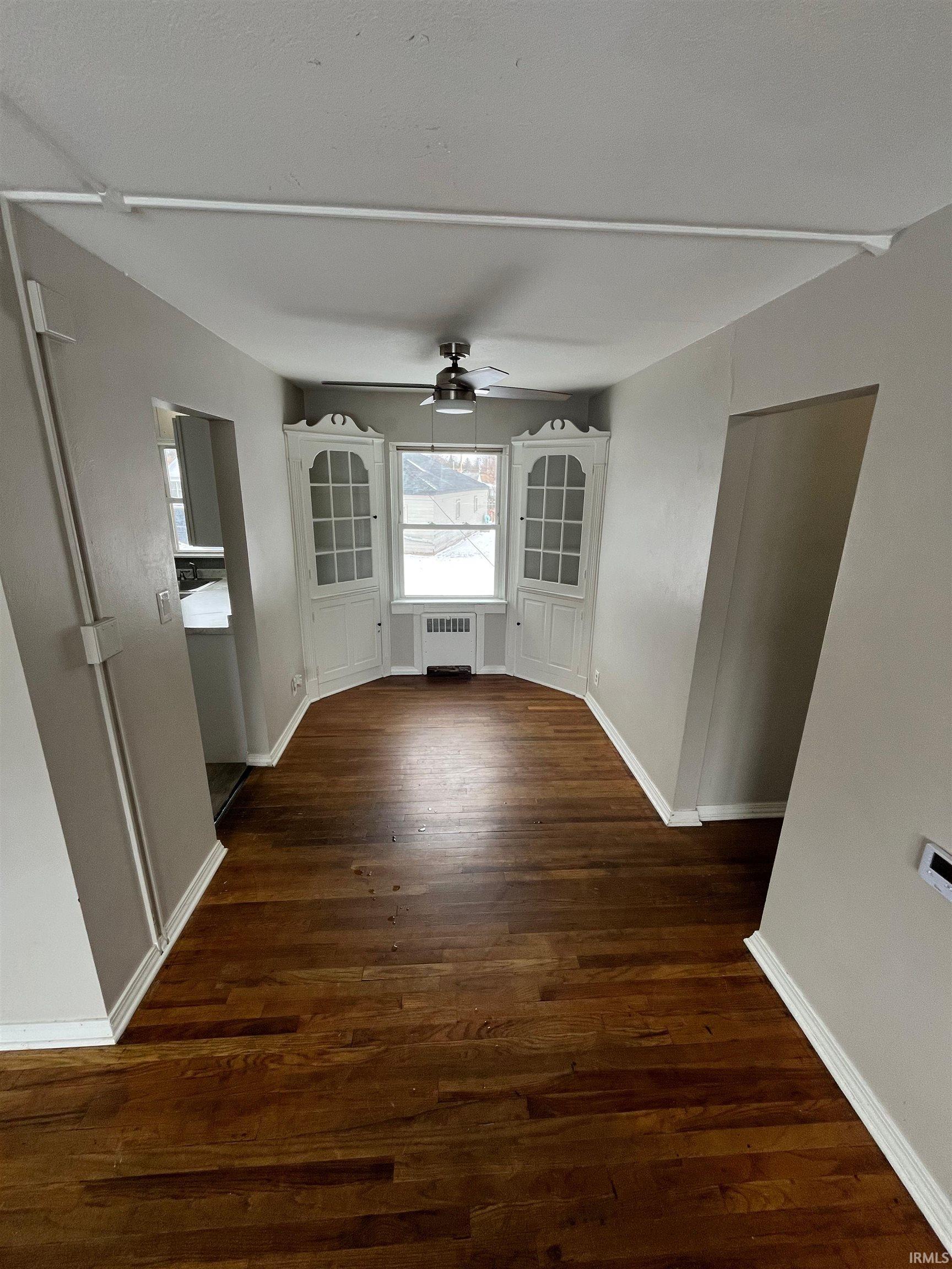 Unfurnished dining area with dark wood-type flooring, ceiling fan, and radiator