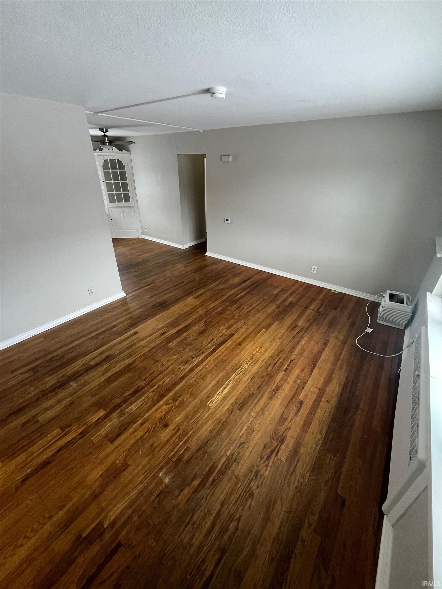 Empty room featuring dark wood-style flooring, a ceiling fan, and a textured ceiling