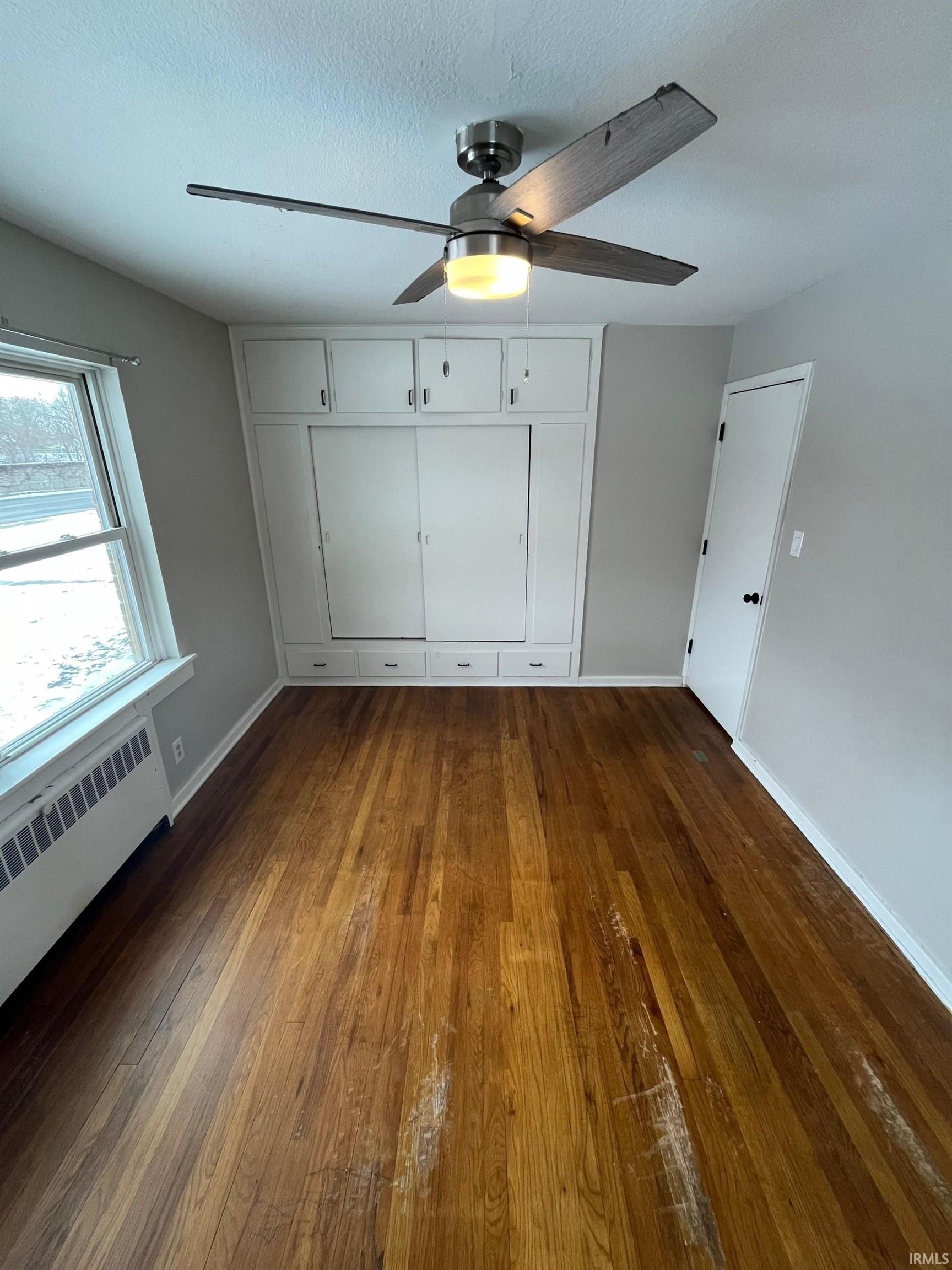 Unfurnished bedroom with radiator, dark wood-style floors, a ceiling fan, a closet, and a textured ceiling