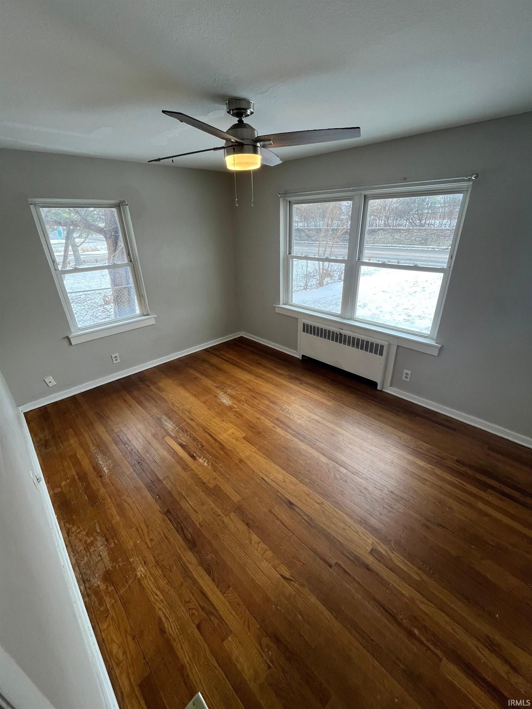 Unfurnished room with dark wood finished floors, radiator heating unit, and a ceiling fan