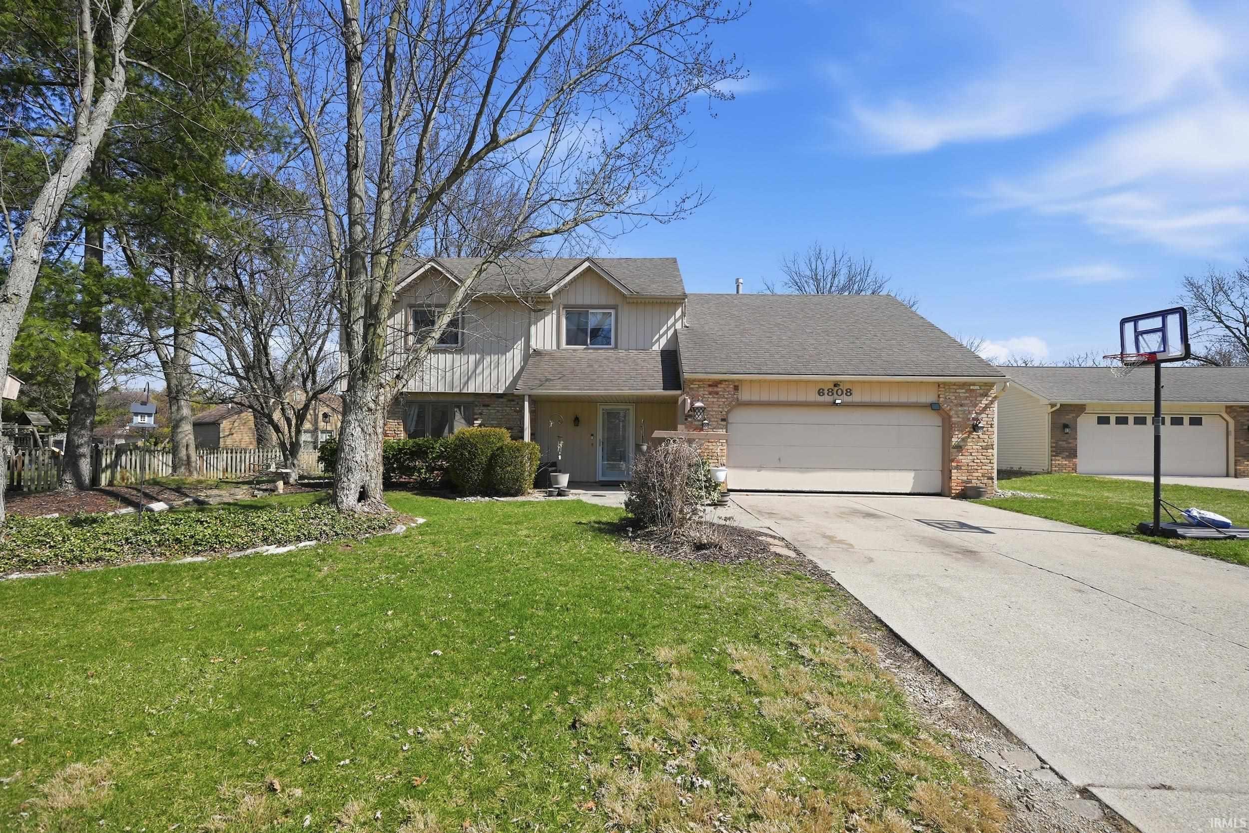 Traditional-style home featuring covered porch, an attached garage, driveway, and a front lawn
