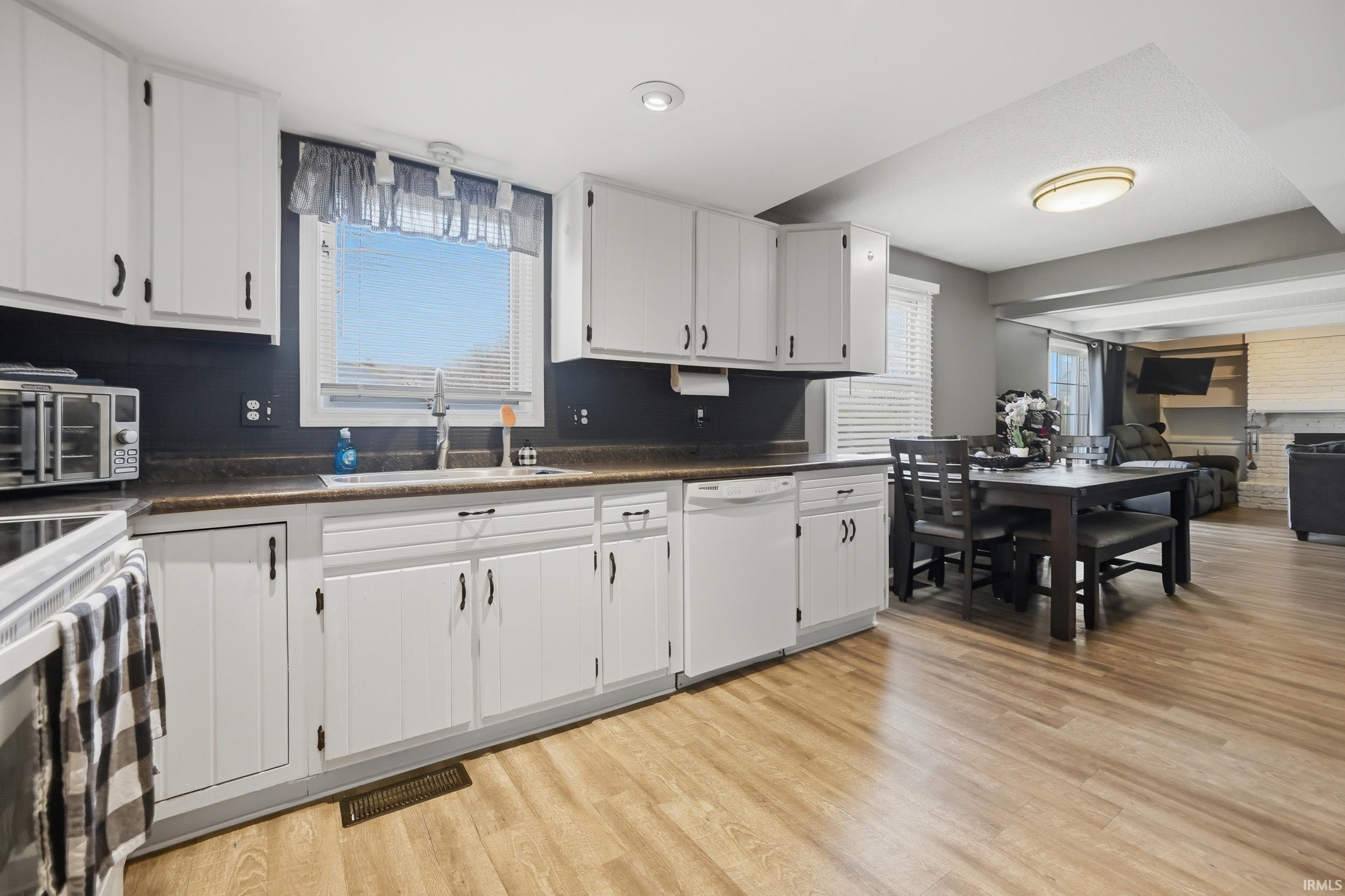Kitchen featuring dark countertops, white appliances, white cabinets, and light wood-type flooring