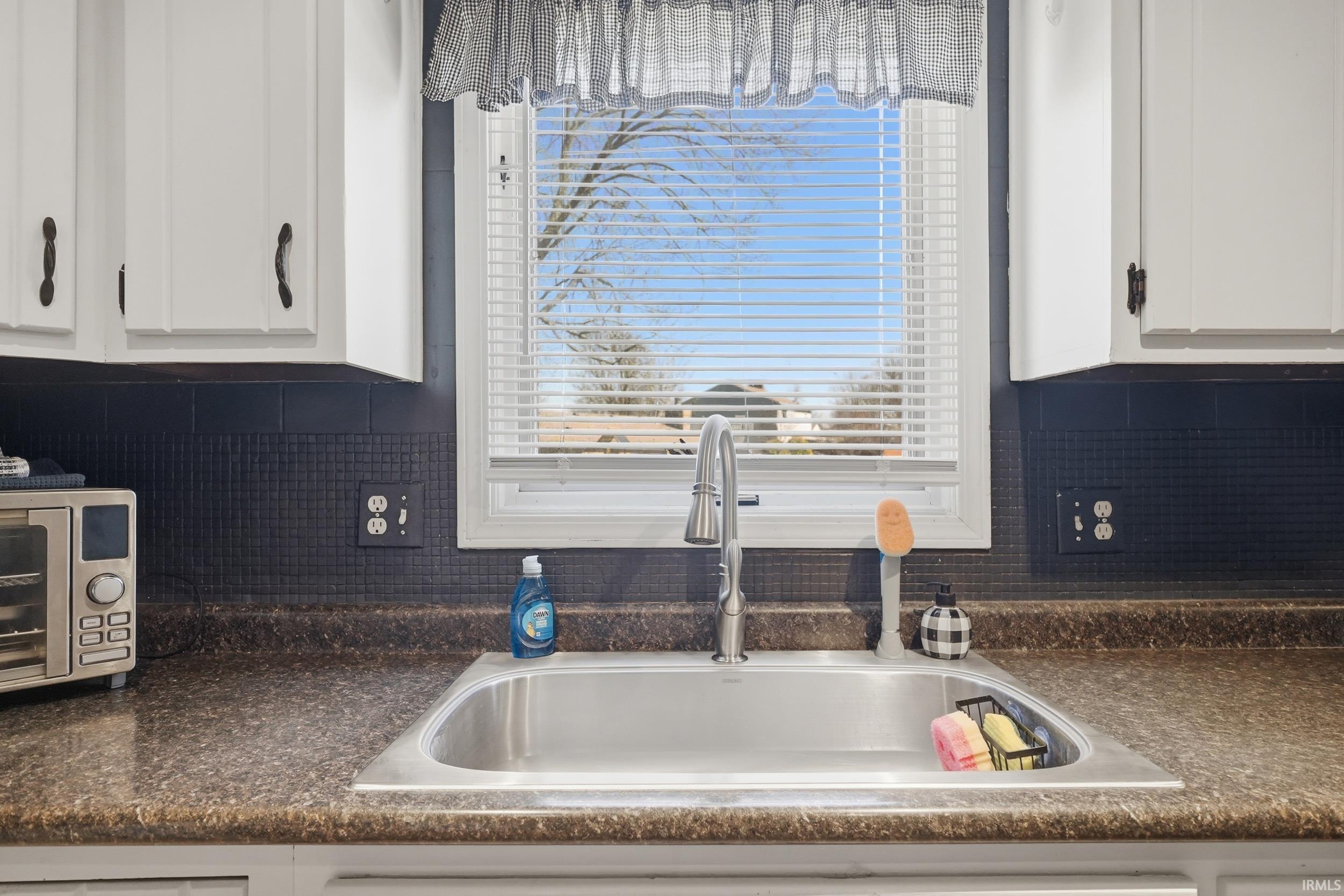 Kitchen featuring white cabinets, dark countertops, and tasteful backsplash
