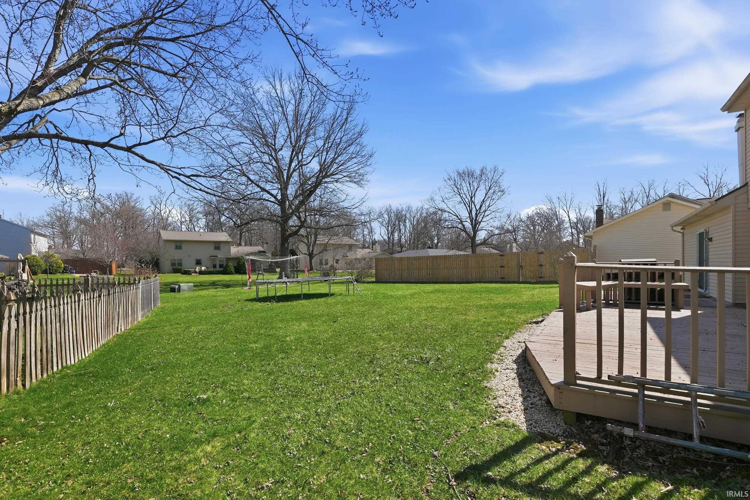 Fenced backyard featuring a trampoline and a wooden deck