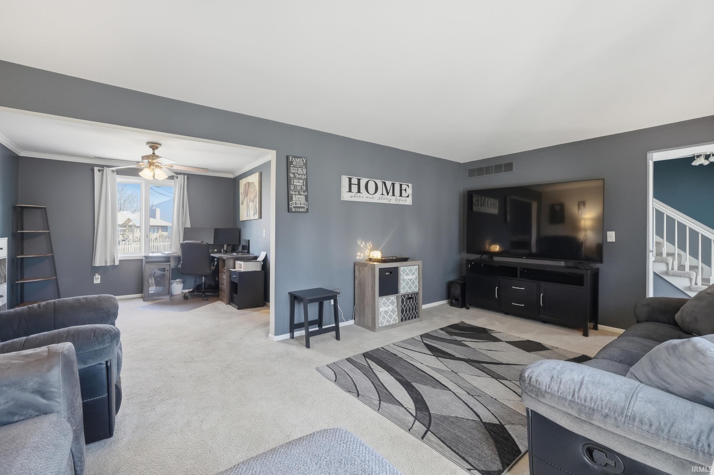 Living area with light colored carpet, ceiling fan, a desk, and ornamental molding