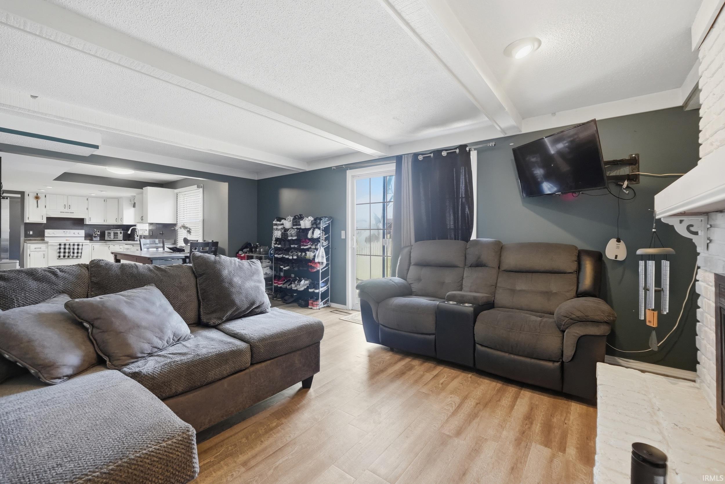 Living room featuring a textured ceiling, light wood-type flooring, and beam ceiling