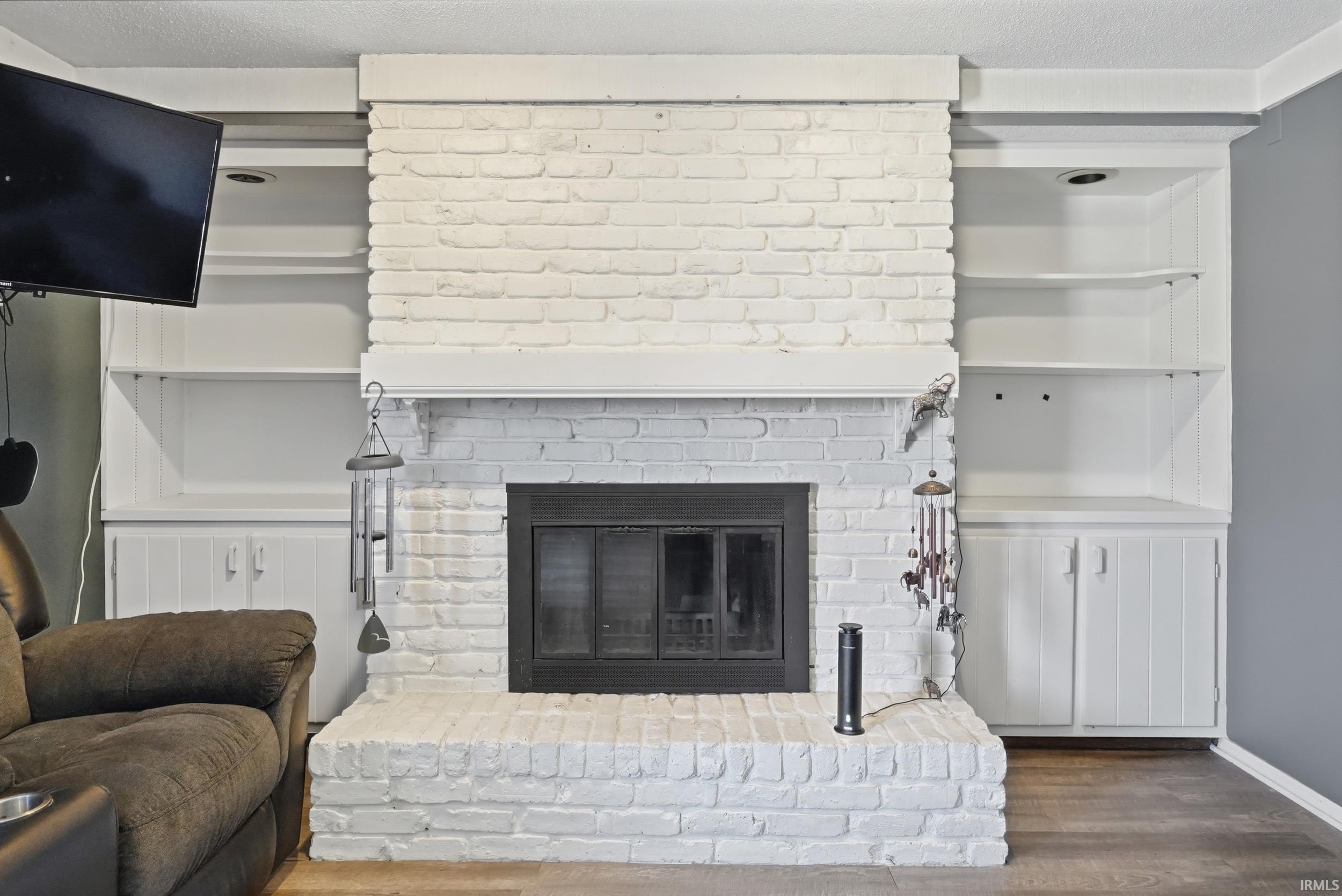 Detailed view of wood finished floors, a brick fireplace, and a textured ceiling