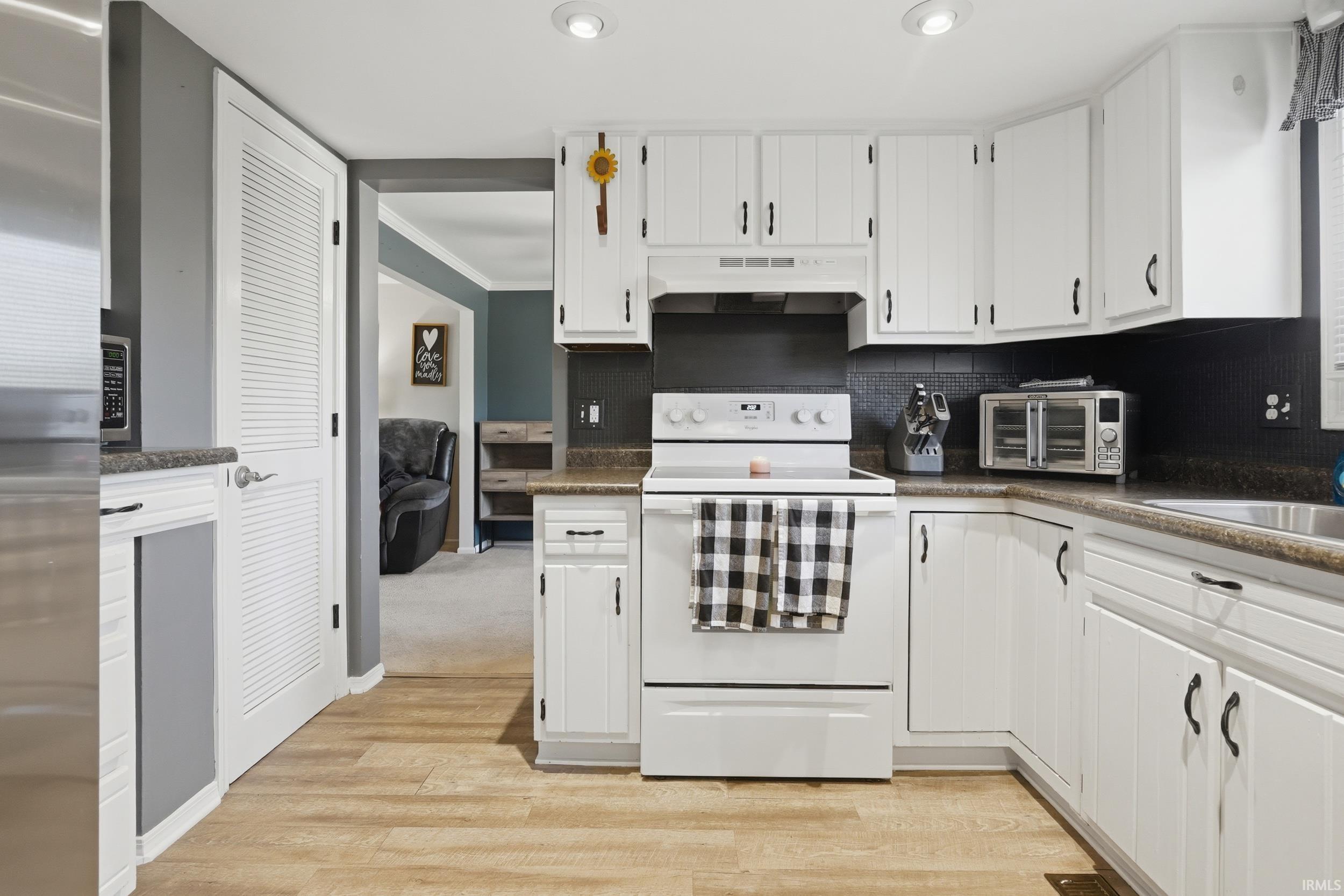 Kitchen with stainless steel appliances, crown molding, white cabinets, dark countertops, and light wood finished floors