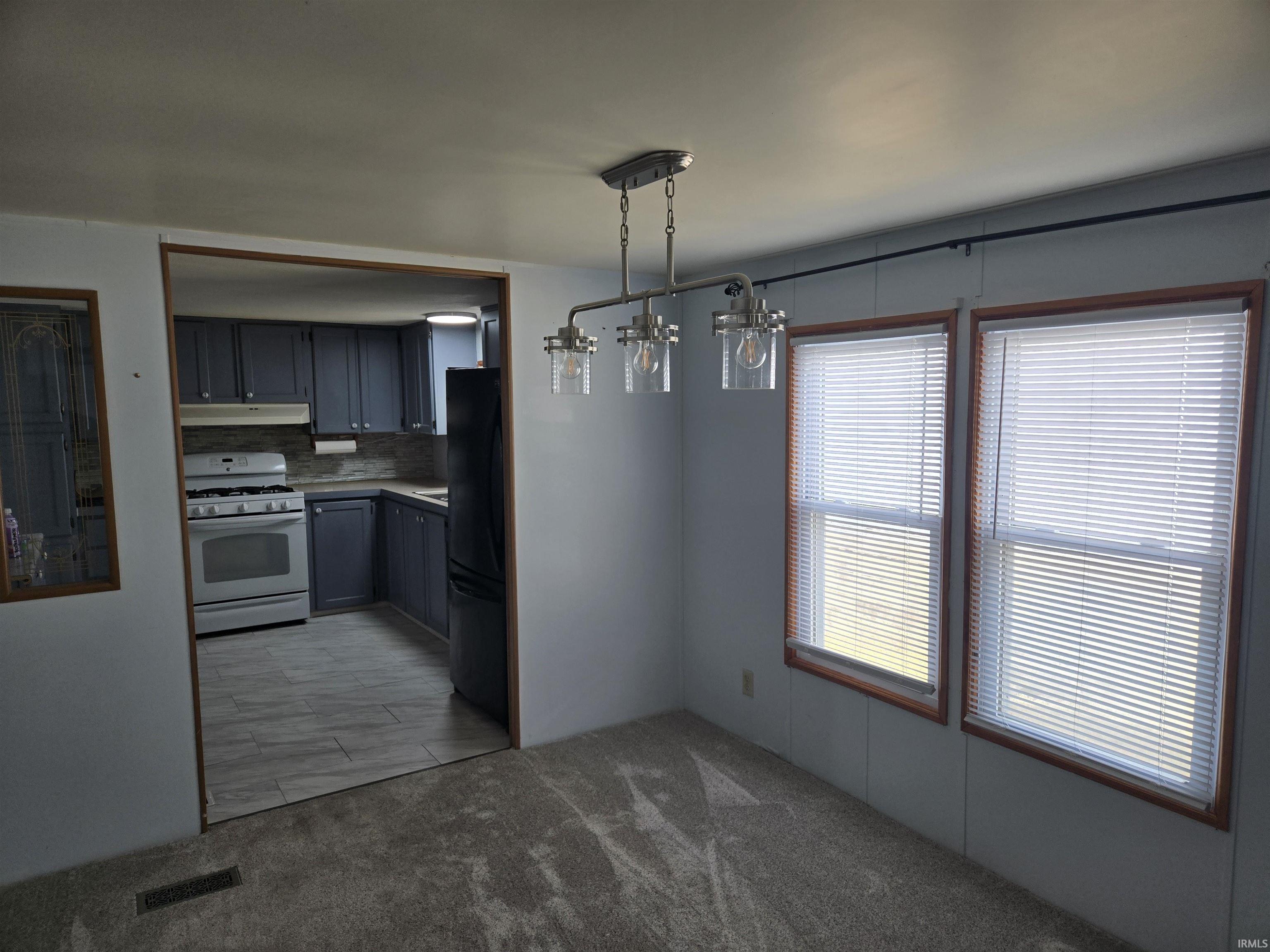 Kitchen featuring white gas stove, gray cabinetry, freestanding refrigerator, hanging light fixtures, and light colored carpet