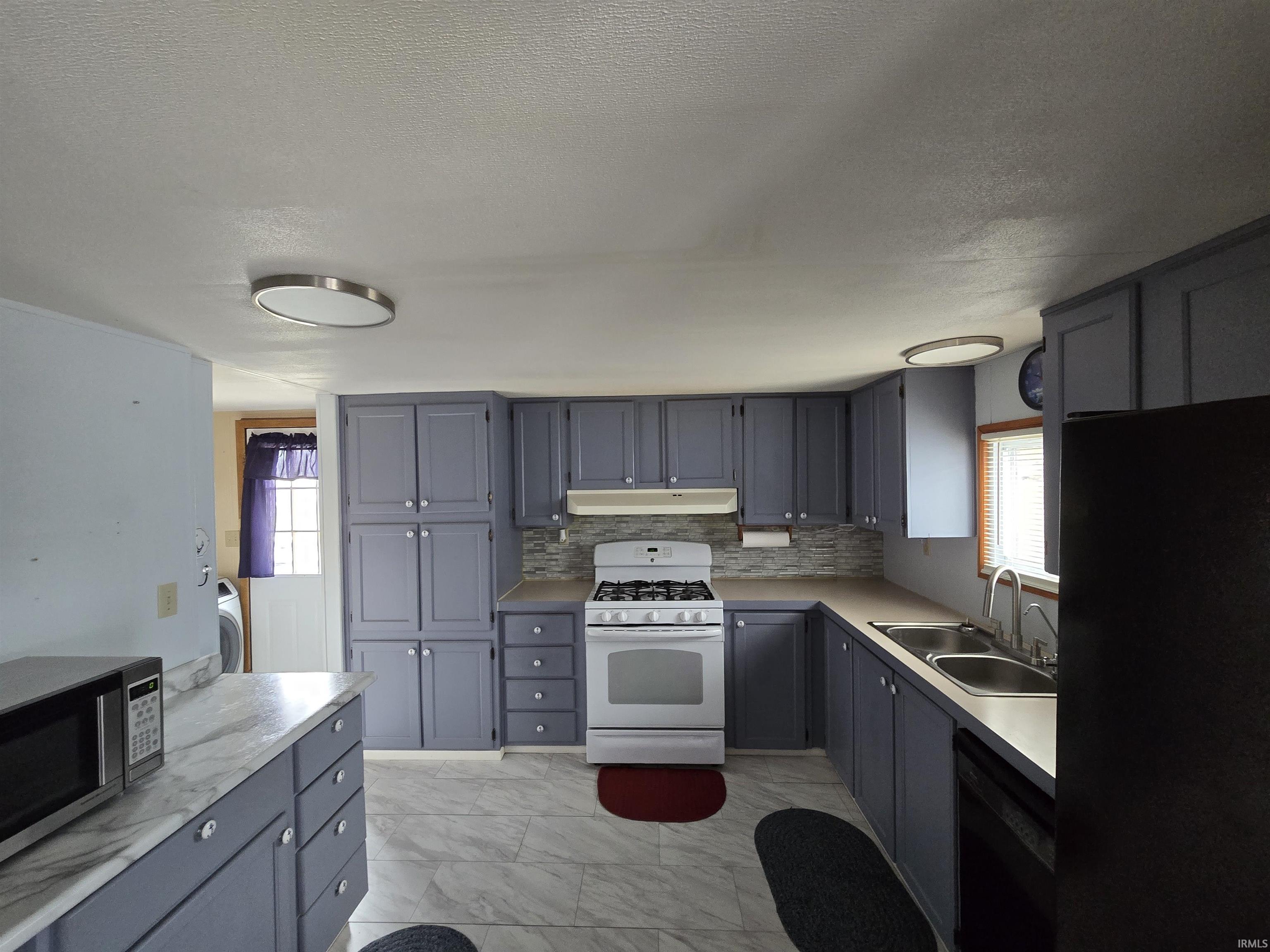 Kitchen with gray cabinetry, black appliances, light countertops, light marble finish floors, and a textured ceiling