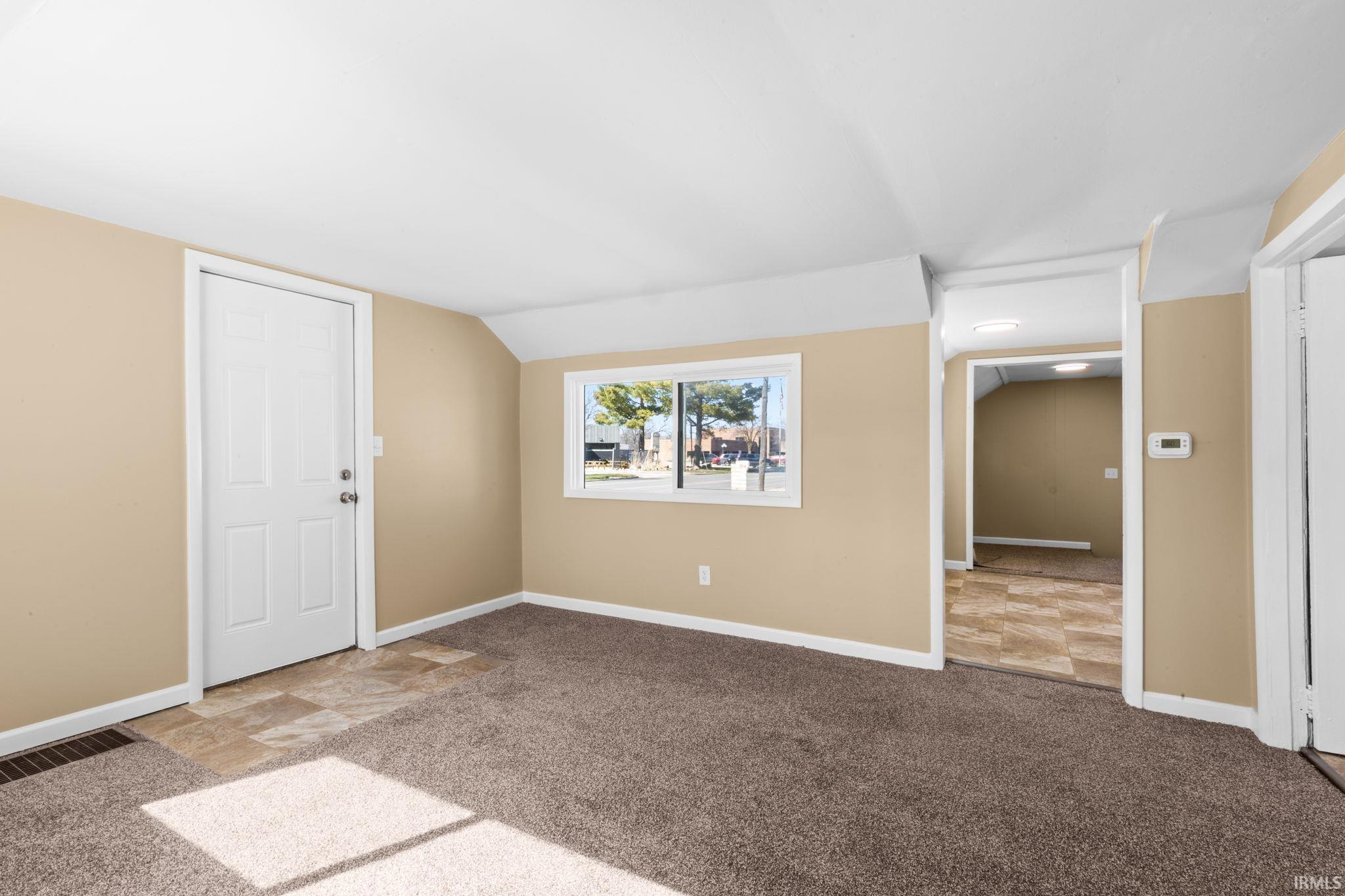 Empty room with light colored carpet and vaulted ceiling