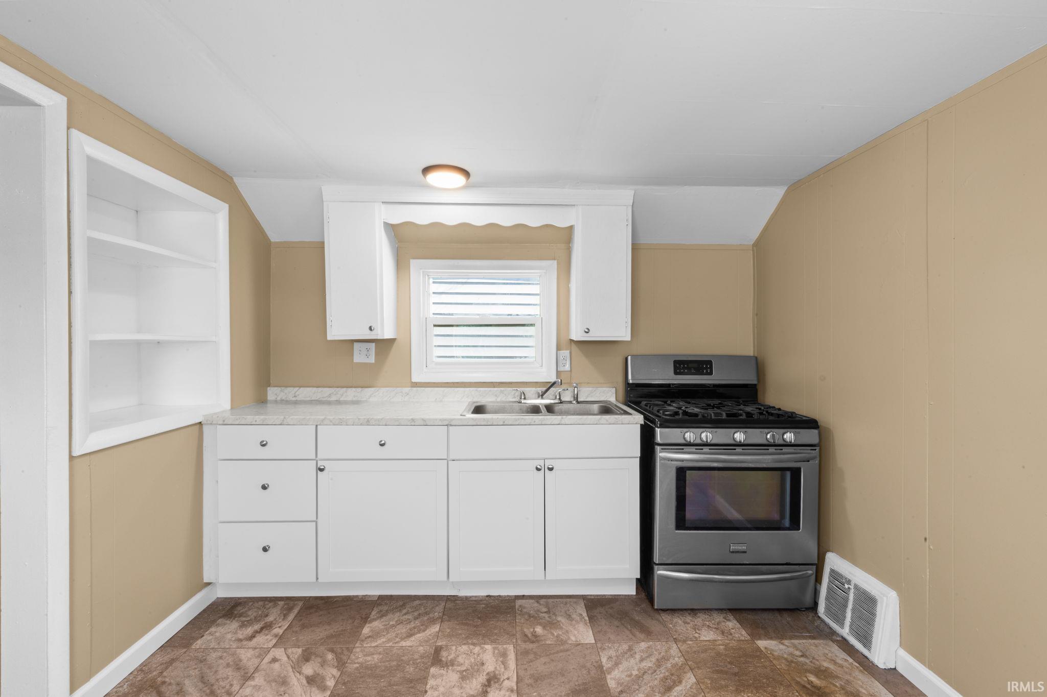 Kitchen featuring white cabinets, stainless steel gas stove, light countertops, lofted ceiling, and stone finish floors