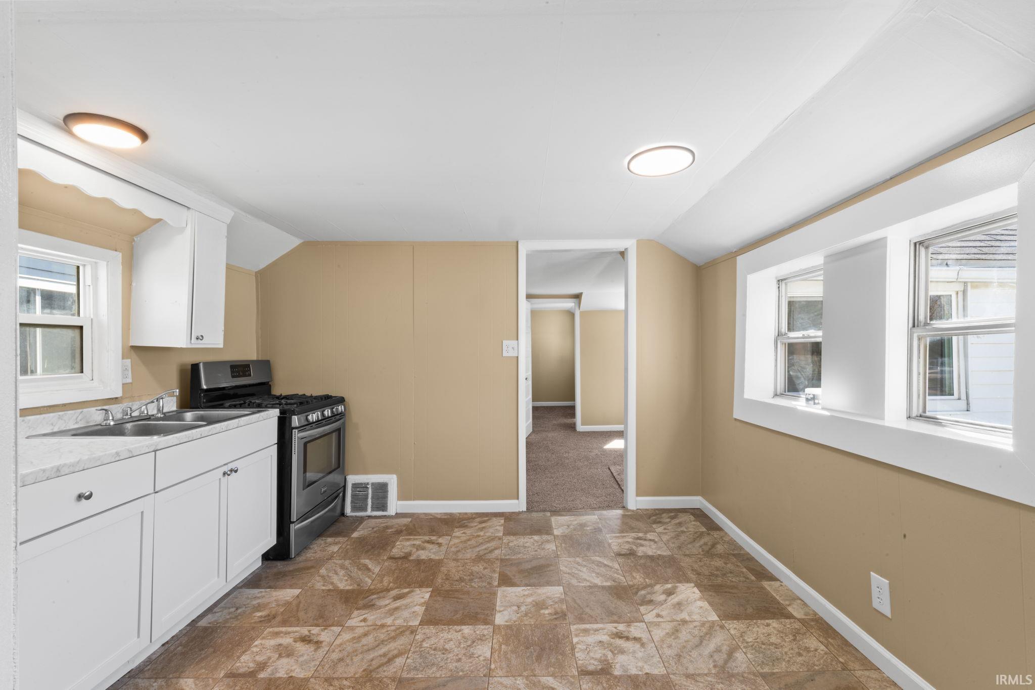 Kitchen with white cabinets, stainless steel gas range oven, stone finish flooring, vaulted ceiling, and light countertops