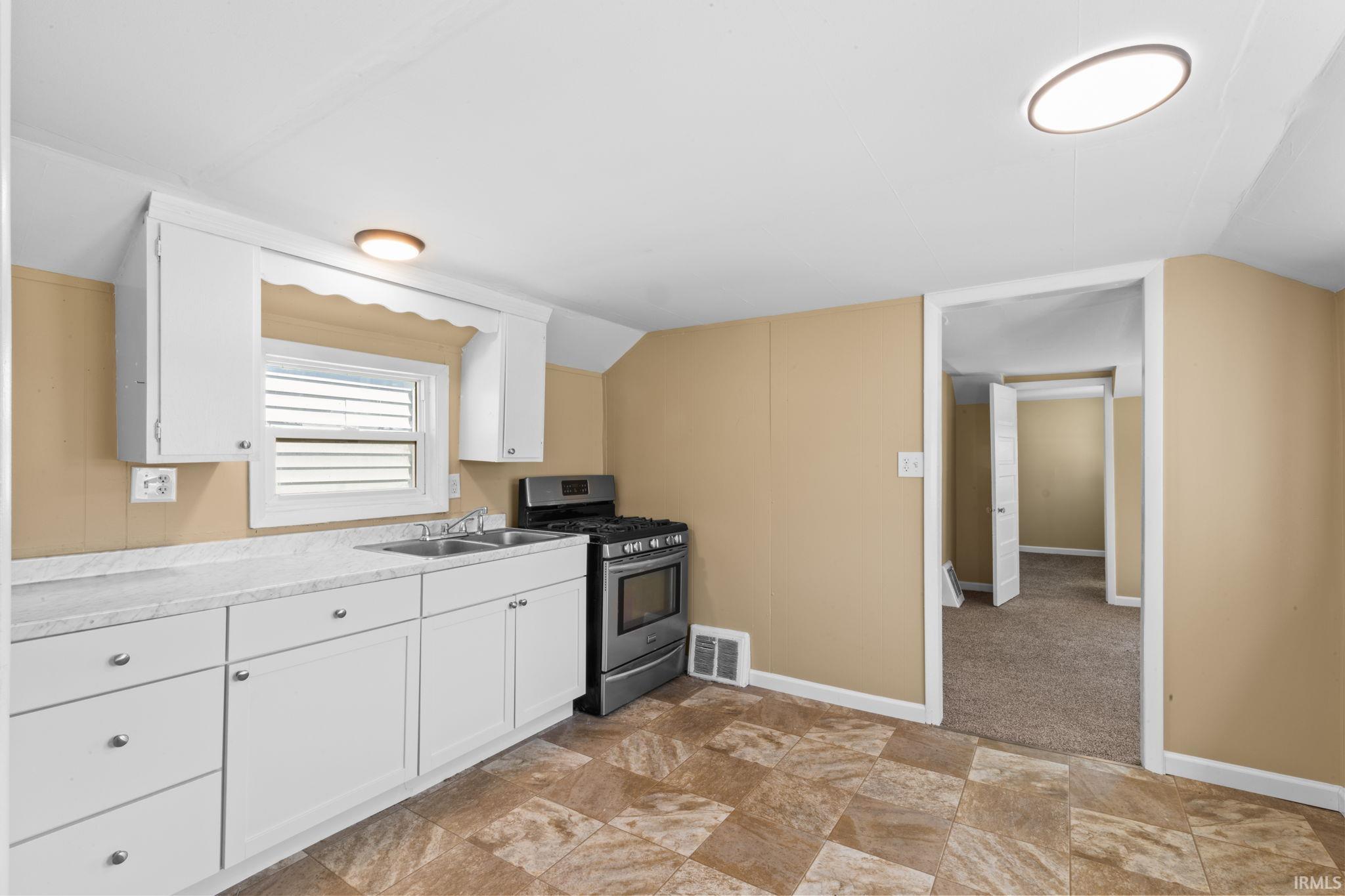 Kitchen with white cabinets, stainless steel gas range, light countertops, lofted ceiling, and stone finish floors