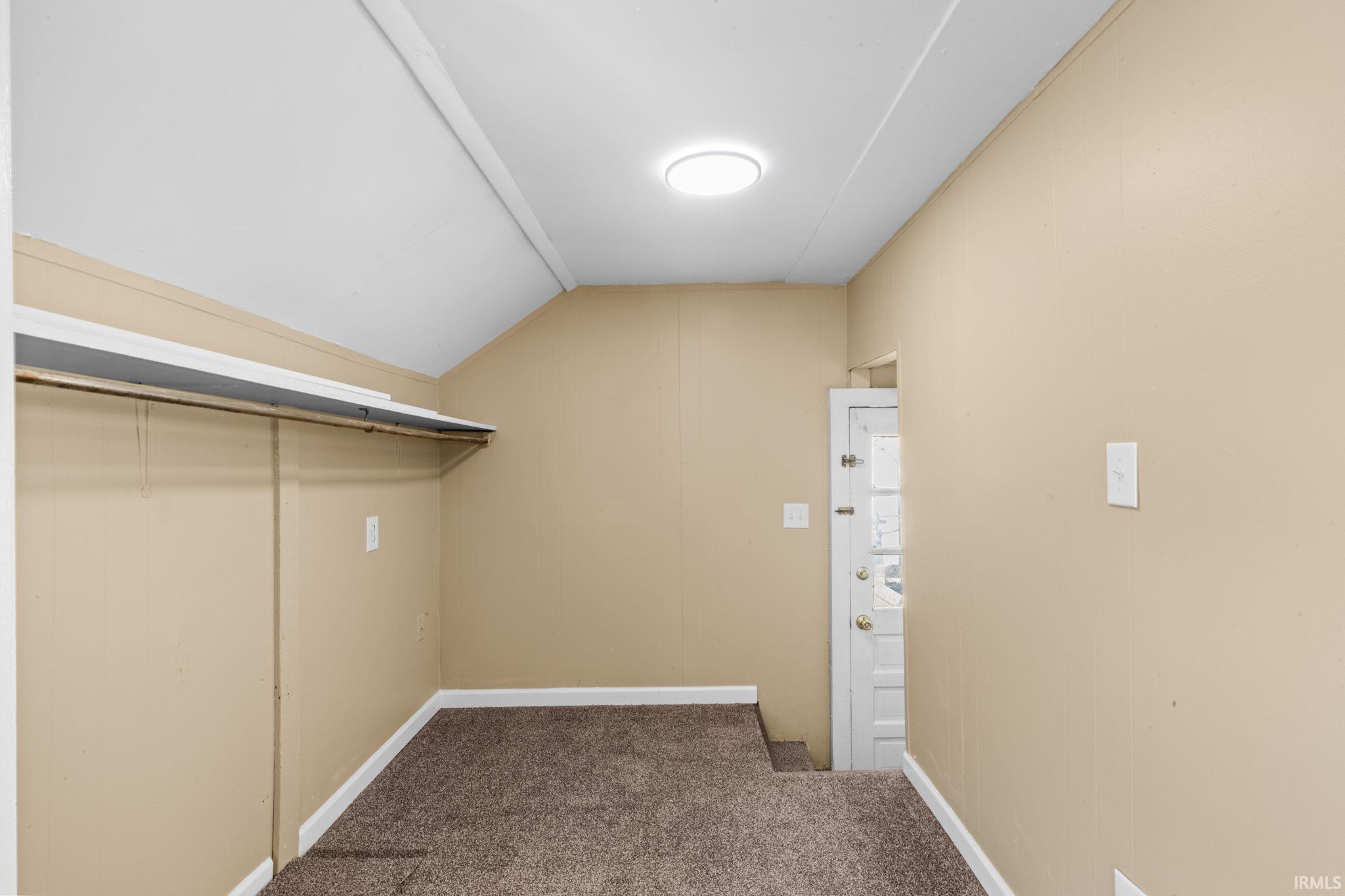 Walk in closet with dark carpet and vaulted ceiling