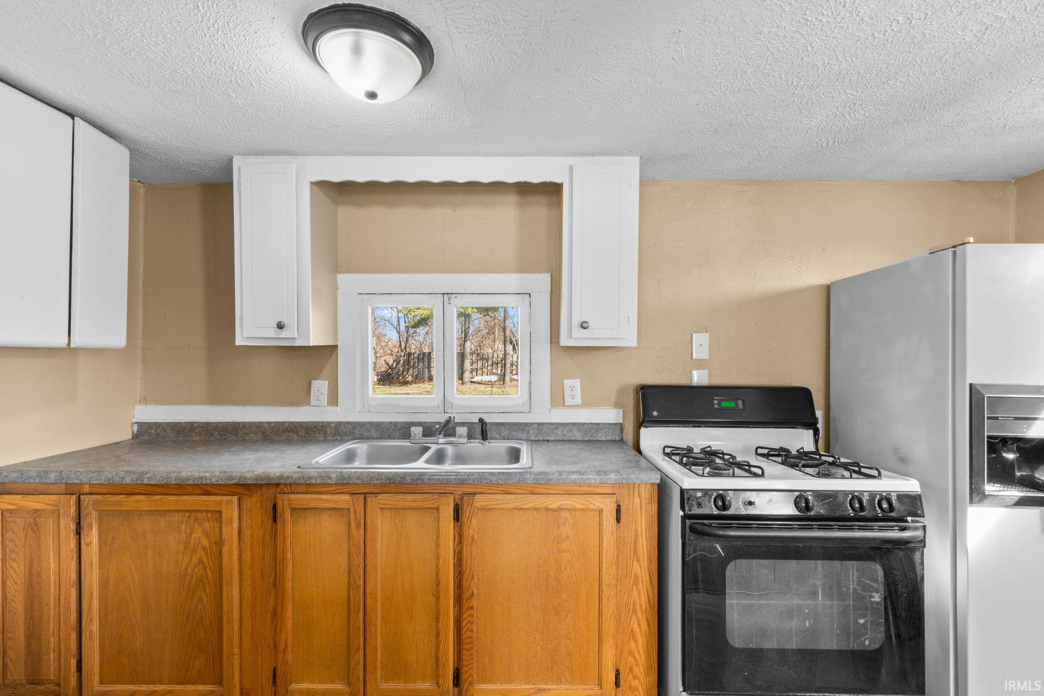 Kitchen with range with gas stovetop, a textured ceiling, and refrigerator with ice dispenser