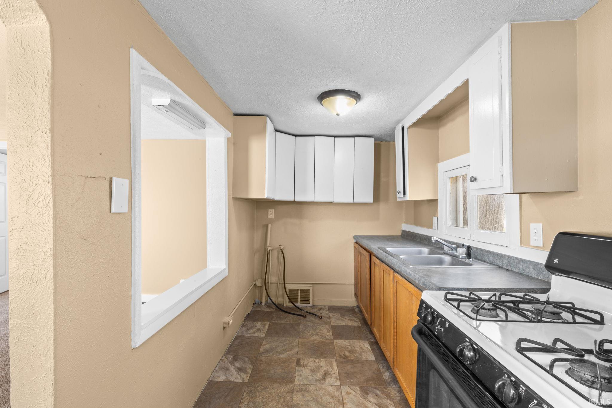 Dual tone kitchen with gas range, dark countertops, dual tone cabinetry, stone finish flooring, and a textured ceiling