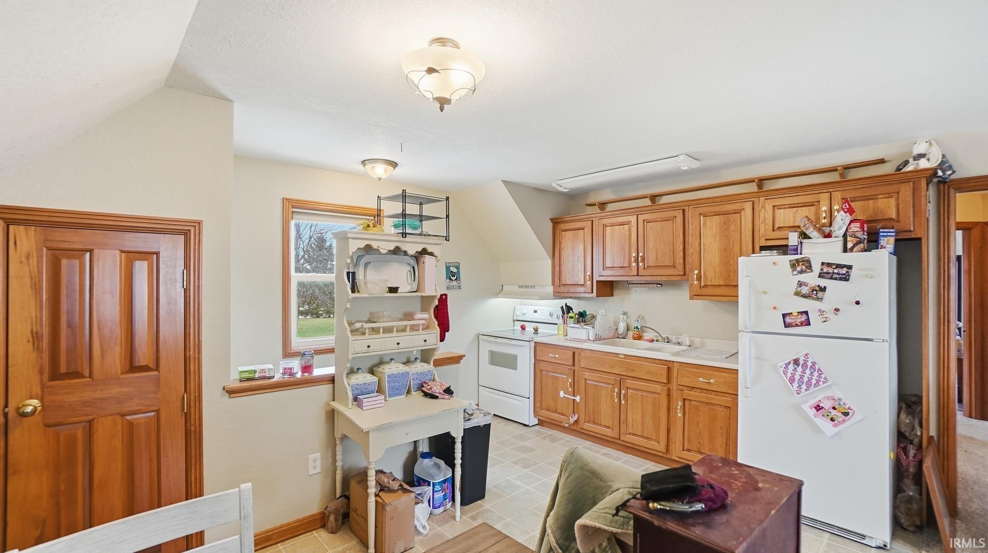 Kitchen with white appliances, light countertops, wood finish cabinetry, and light flooring
