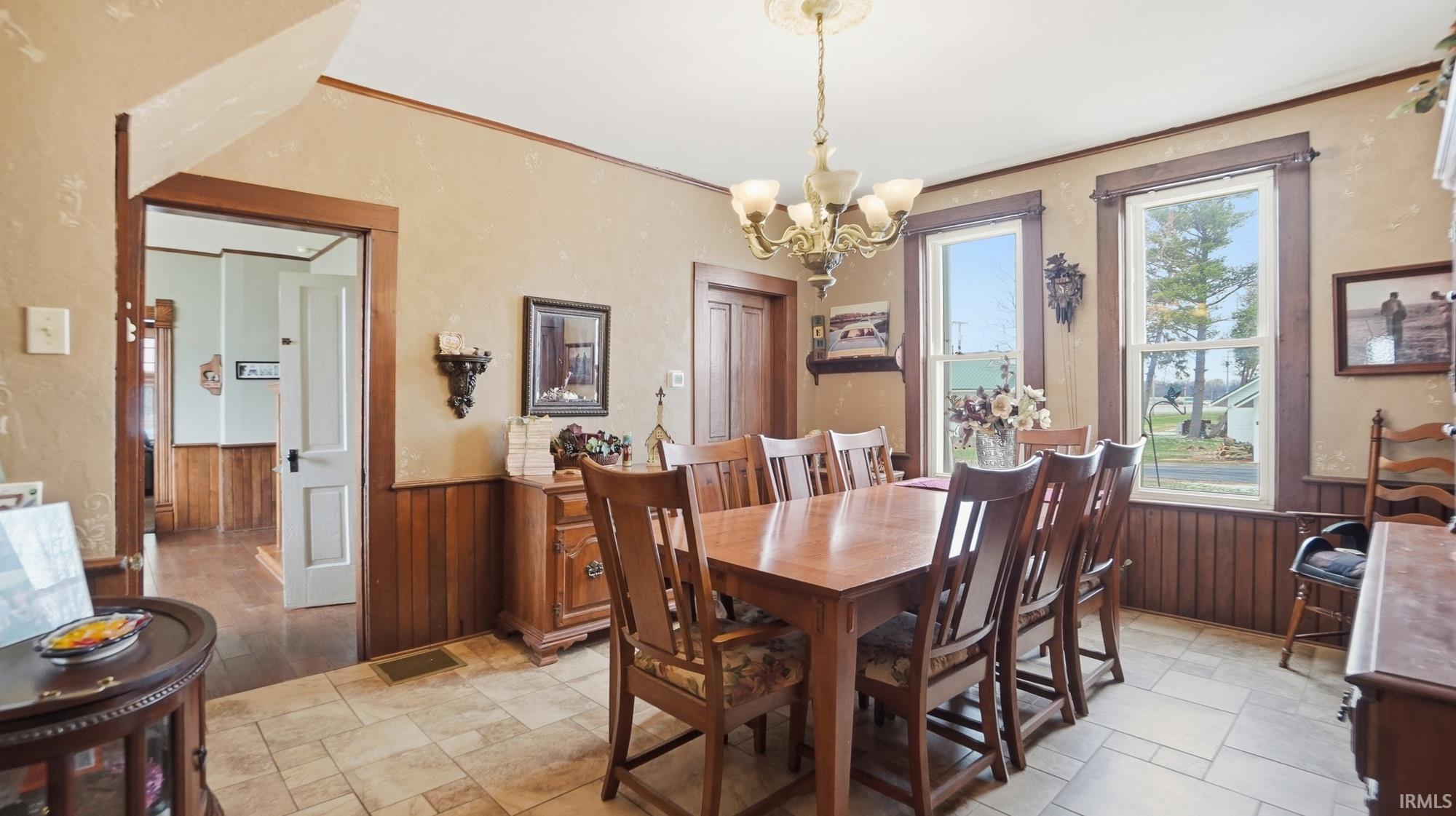 Dining space with a wainscoted wall, wooden walls, suspended lighting, light stone finish flooring, and crown molding