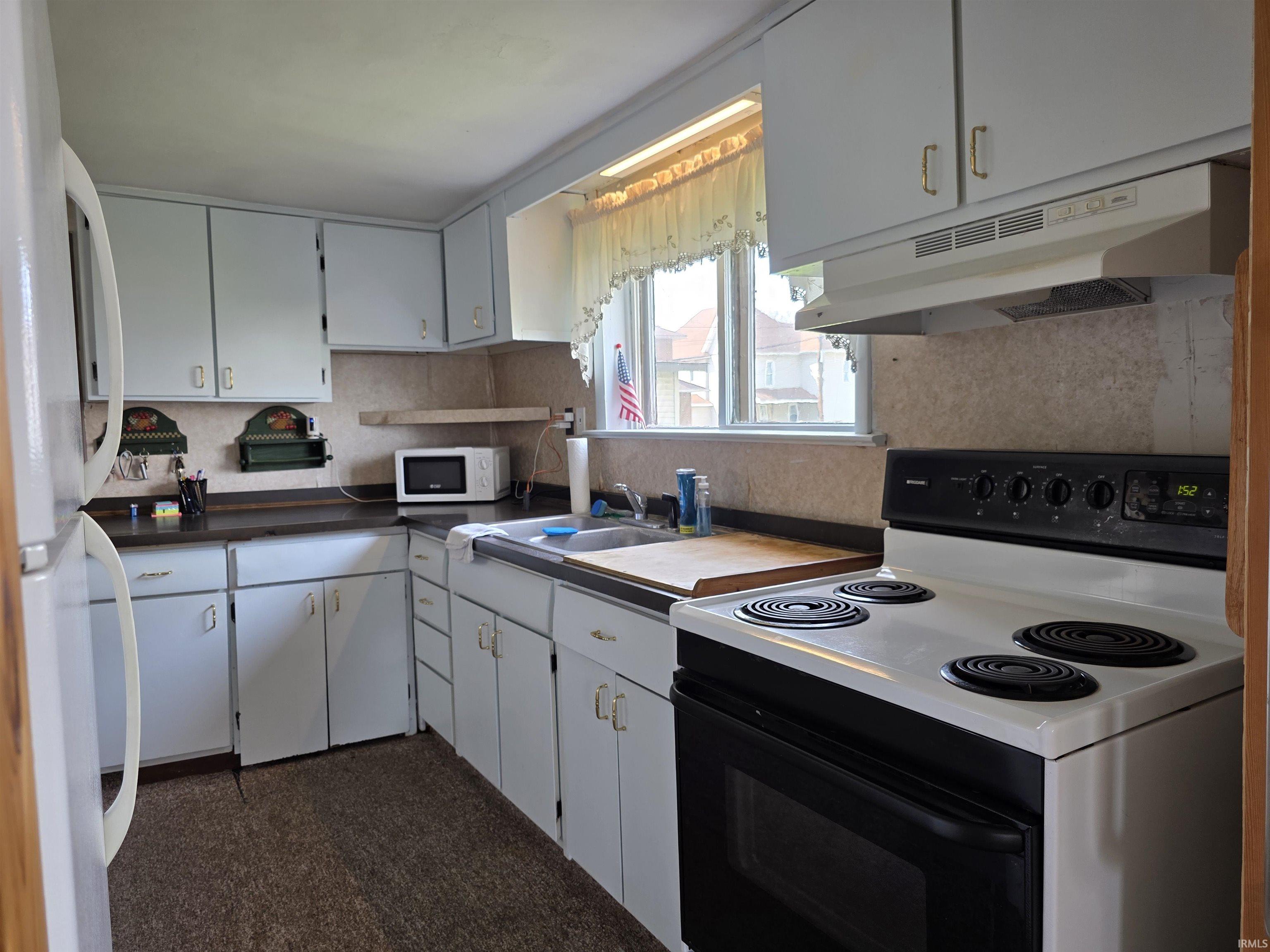 Kitchen with white appliances, dark countertops, and white cabinets