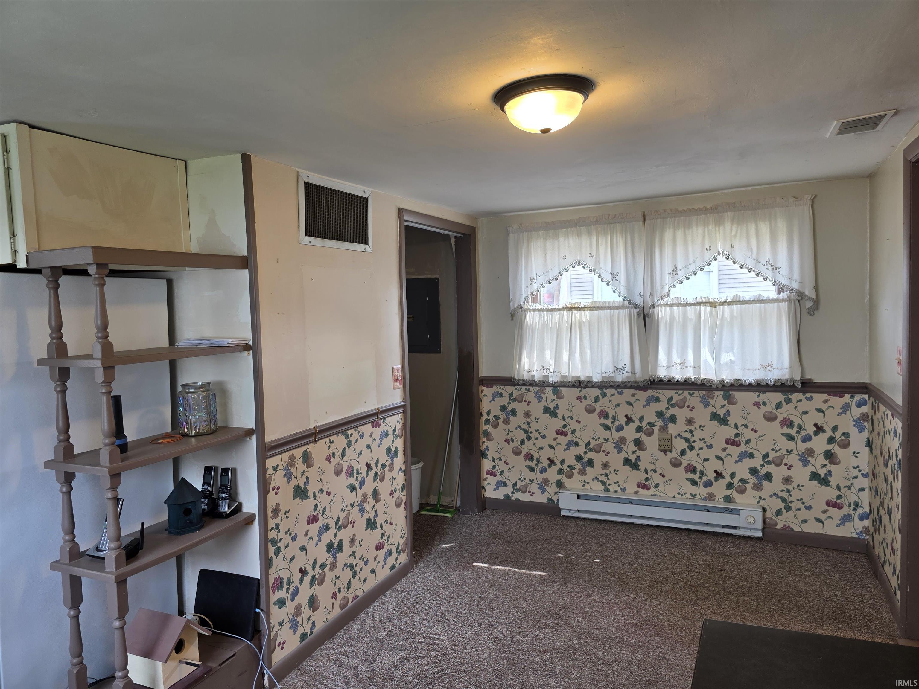 Empty room with wallpapered walls, a baseboard radiator, wainscoting, and dark colored carpet
