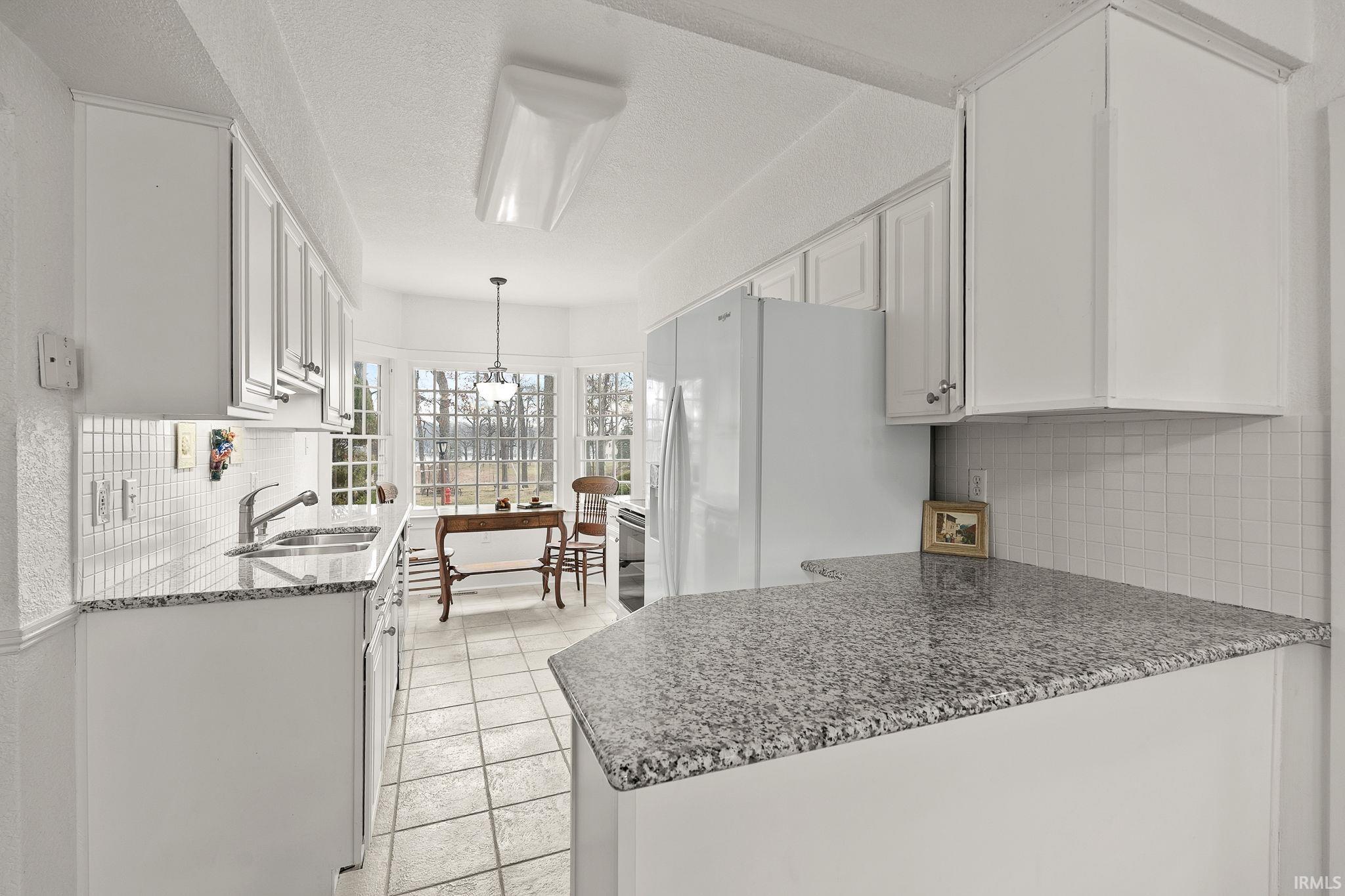 Kitchen with white cabinets, decorative backsplash, white fridge with ice dispenser, a textured ceiling, and dark stone countertops